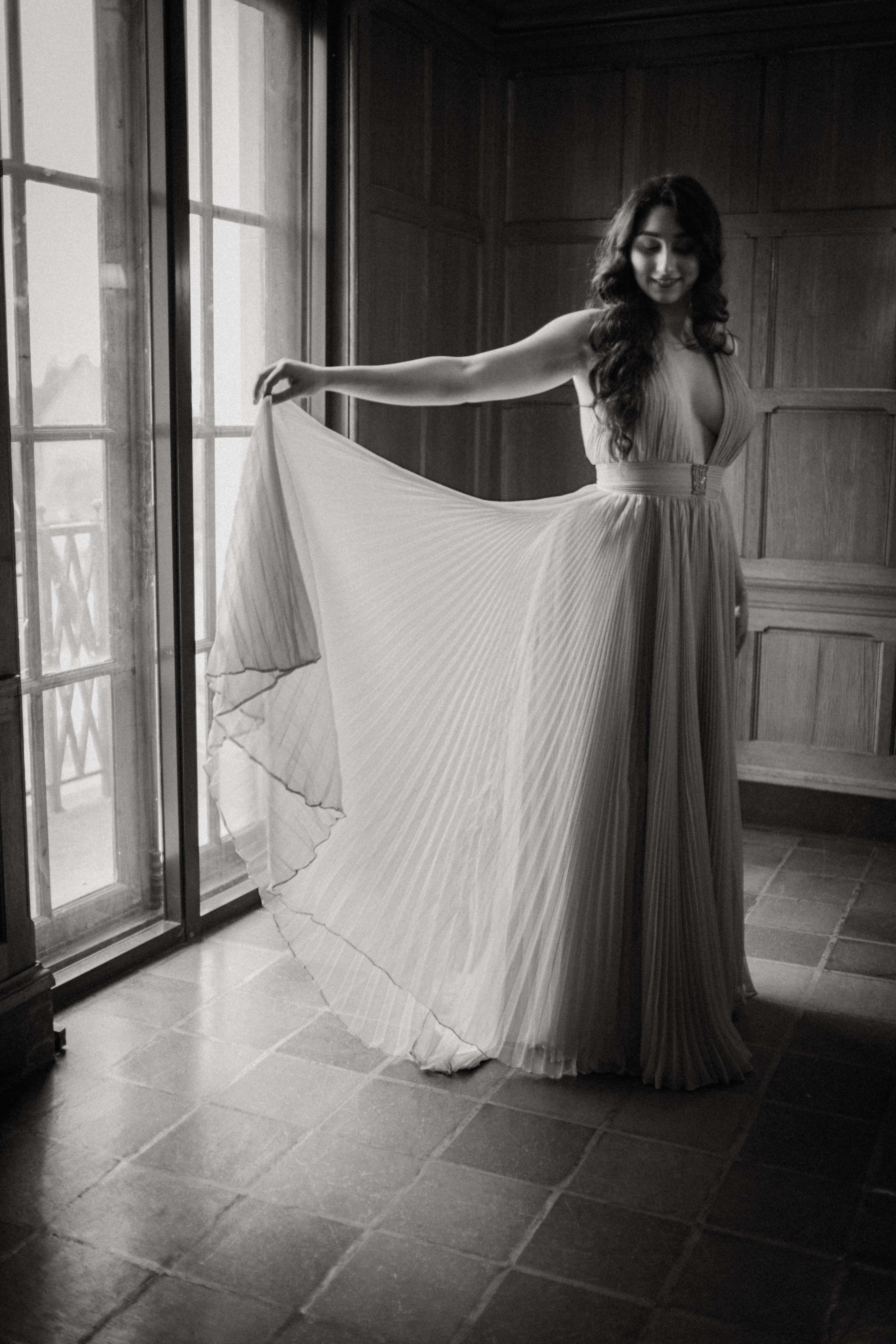a woman in a long dress standing in front of a window