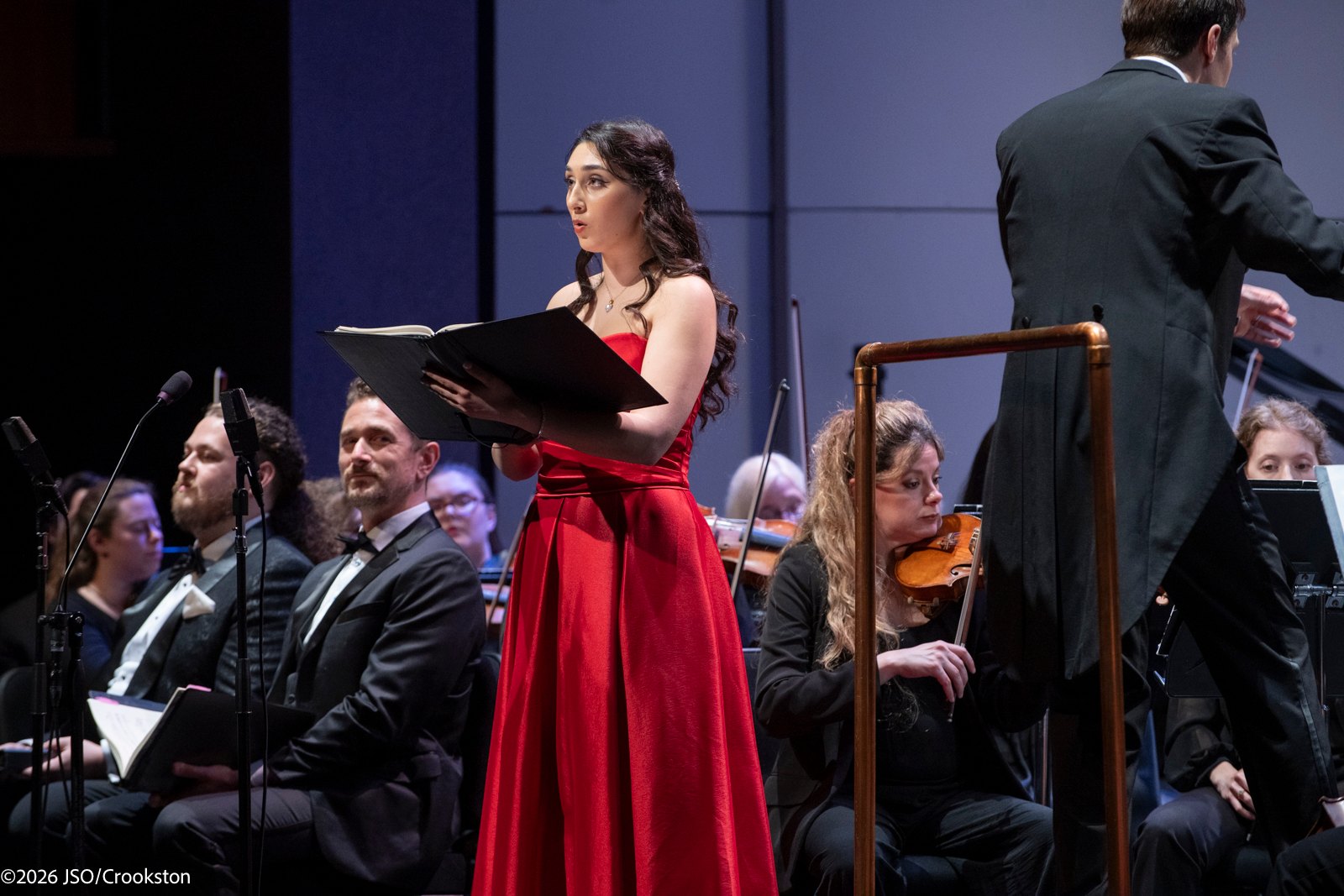a woman in a red dress is standing in front of an orchestra