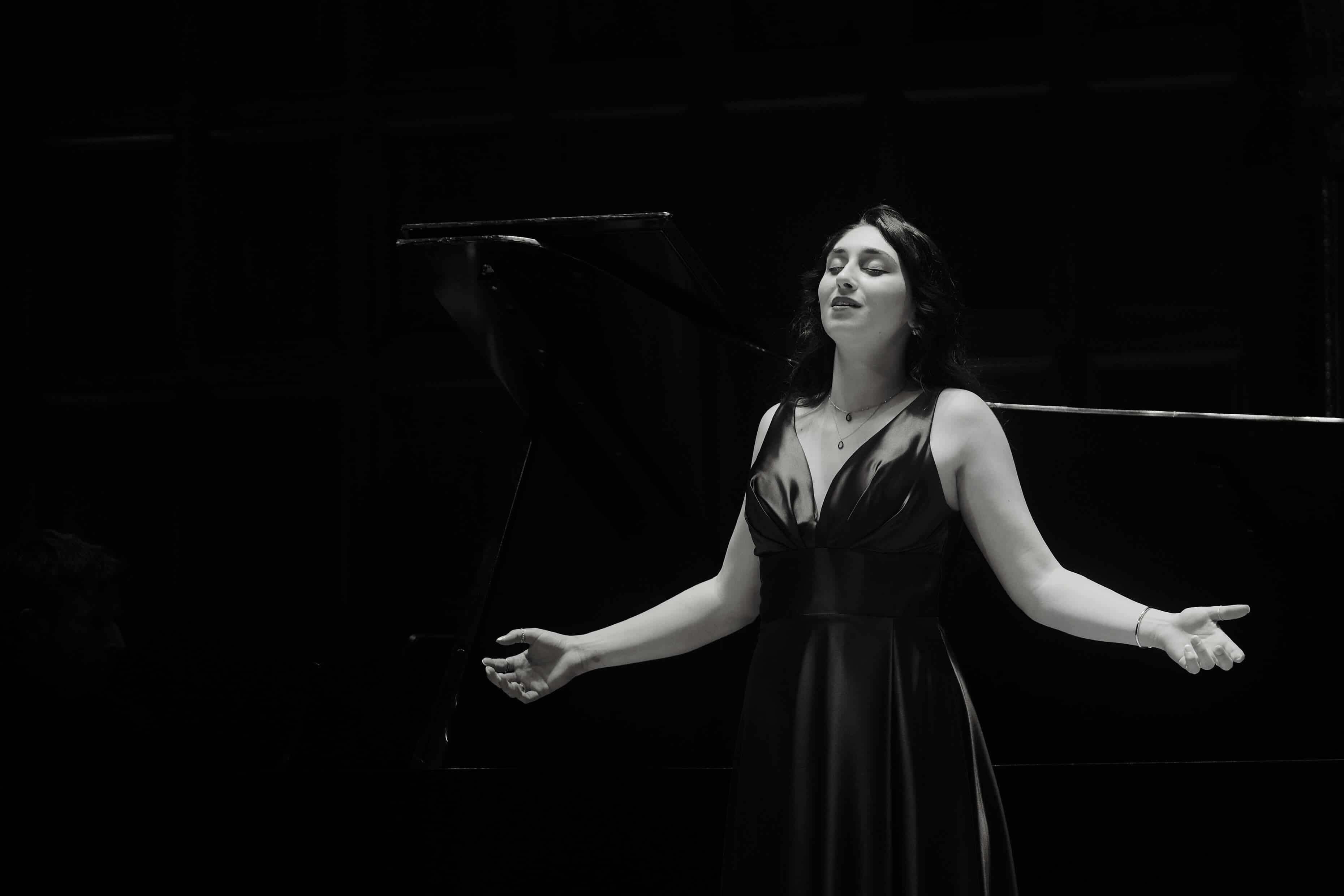 a woman in a black dress singing in front of a piano