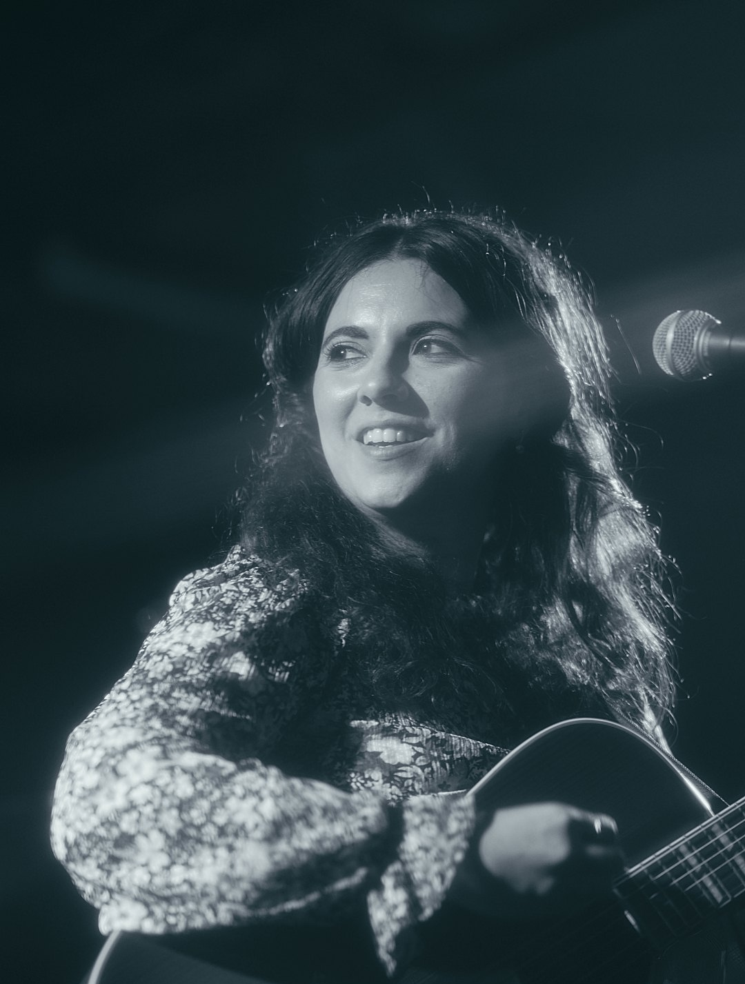 a woman holding an acoustic guitar in front of a microphone