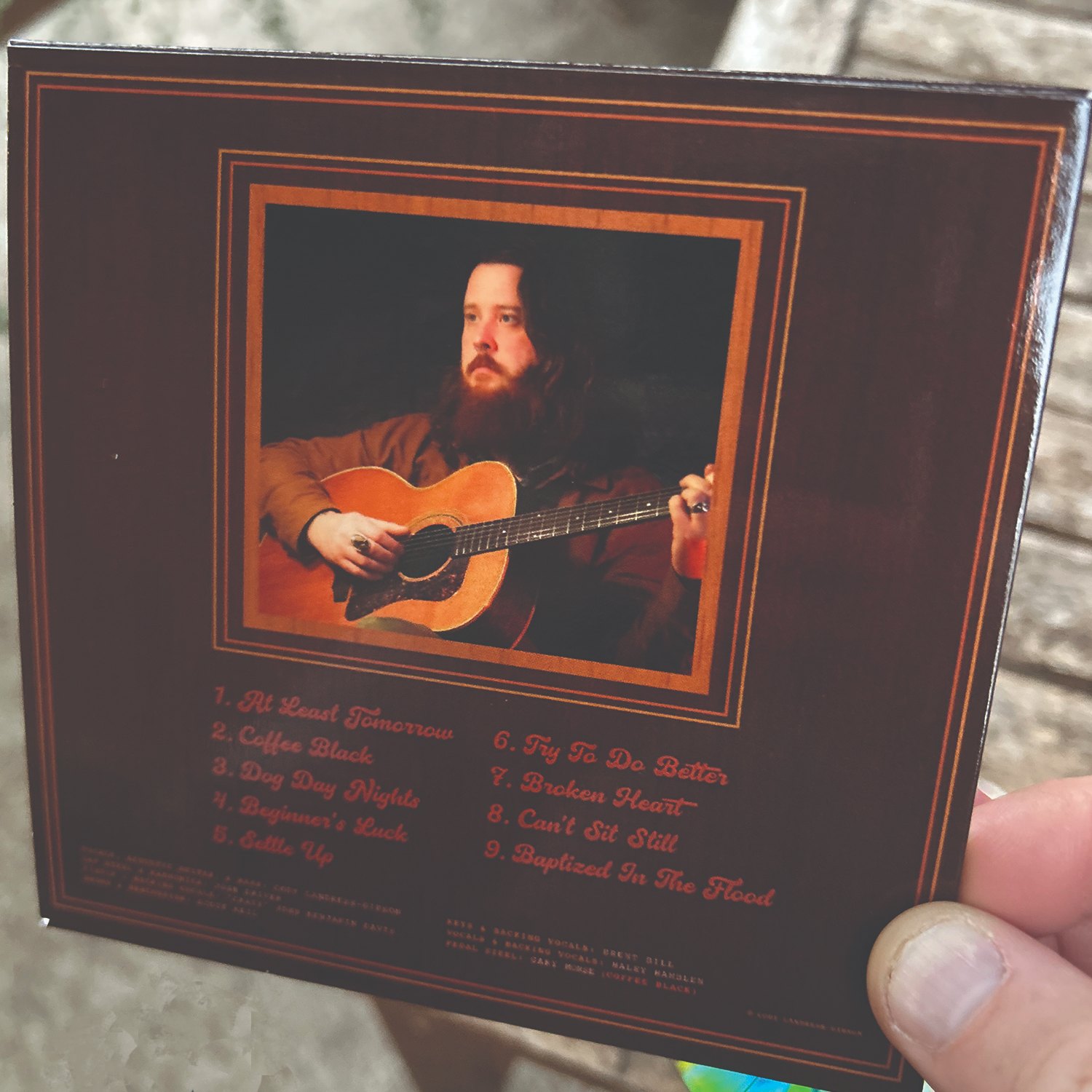 a person holding a cd with a picture of a man playing an acoustic guitar
