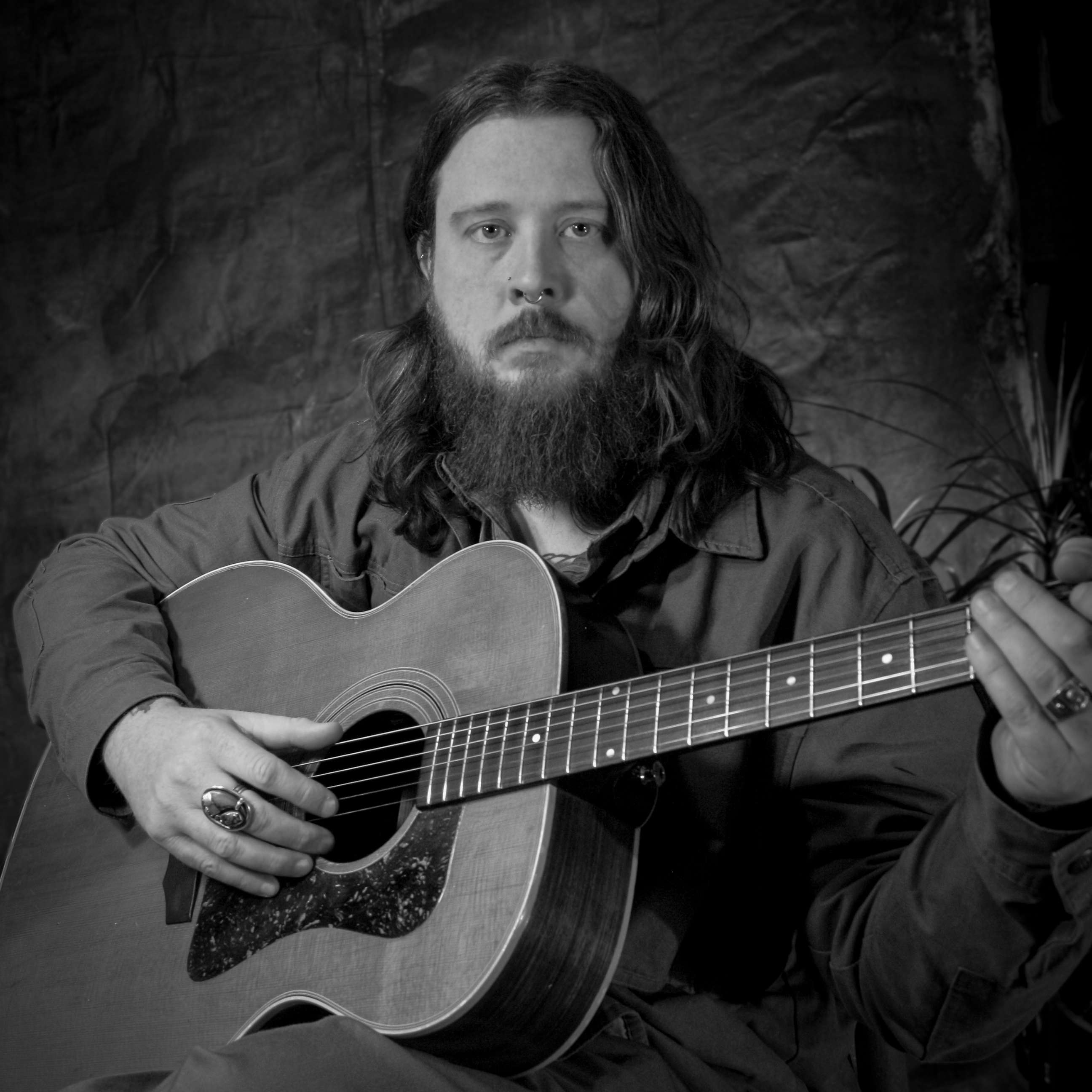 a black and white photo of a bearded man holding an acoustic guitar