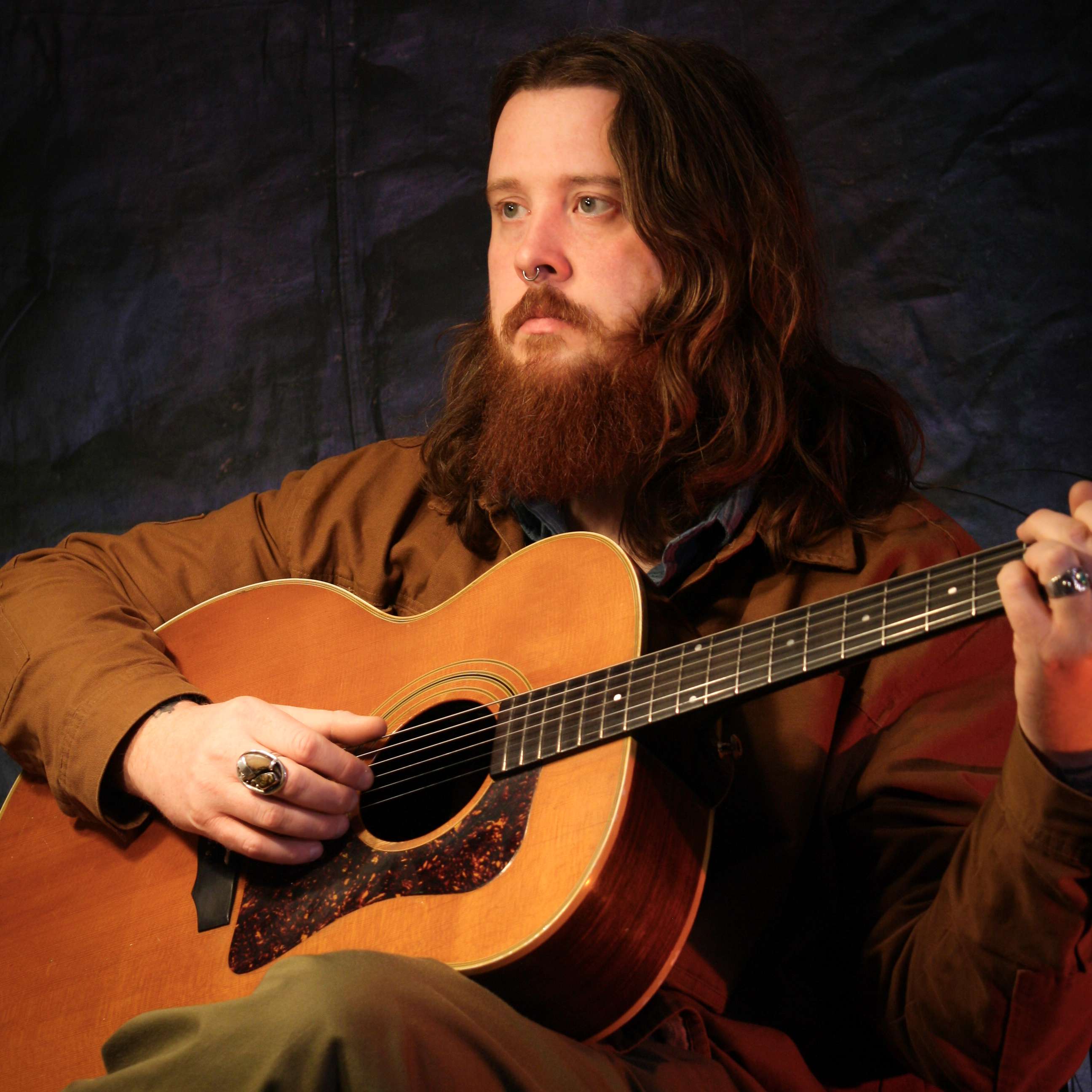 a man with a beard playing an acoustic guitar