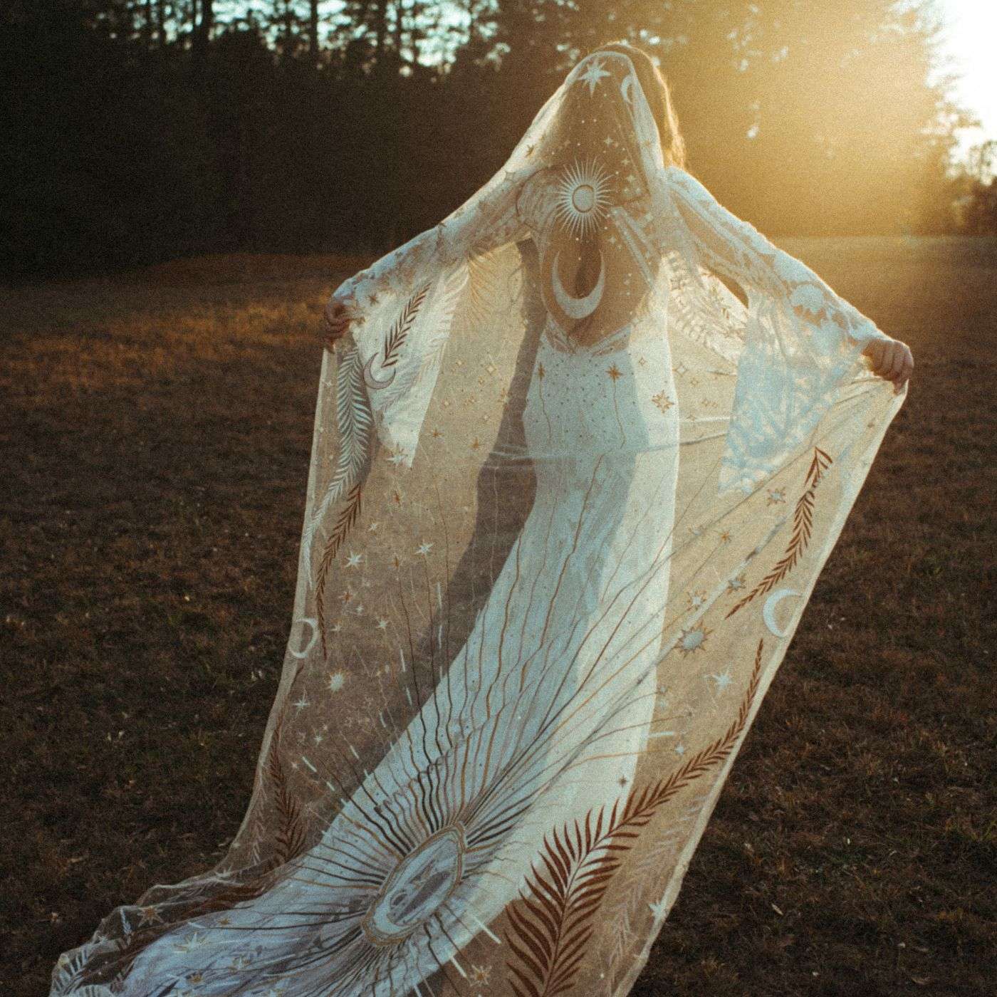 a bride wearing a veil in a field at sunset