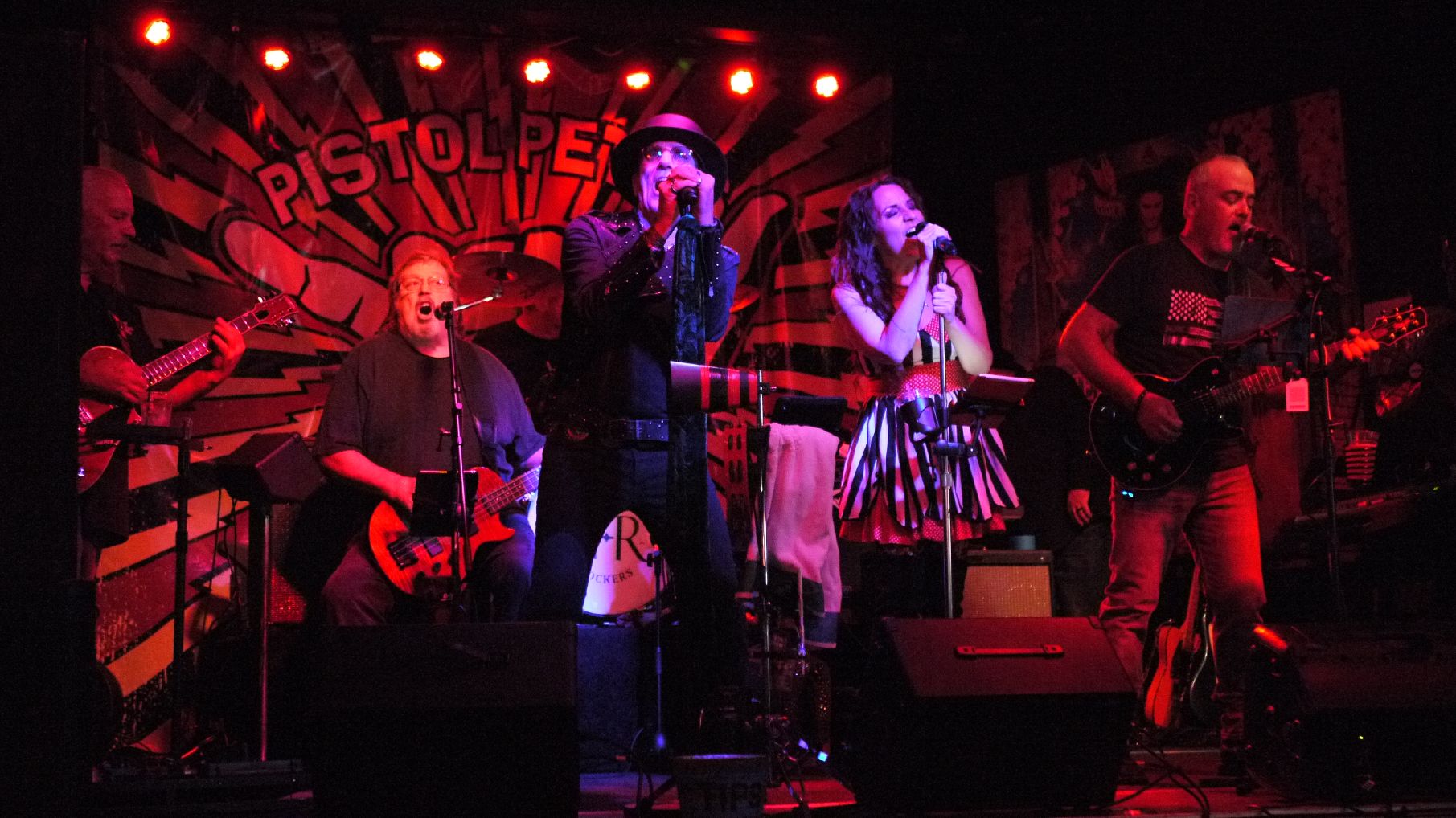 a group of people singing on stage in front of a red light