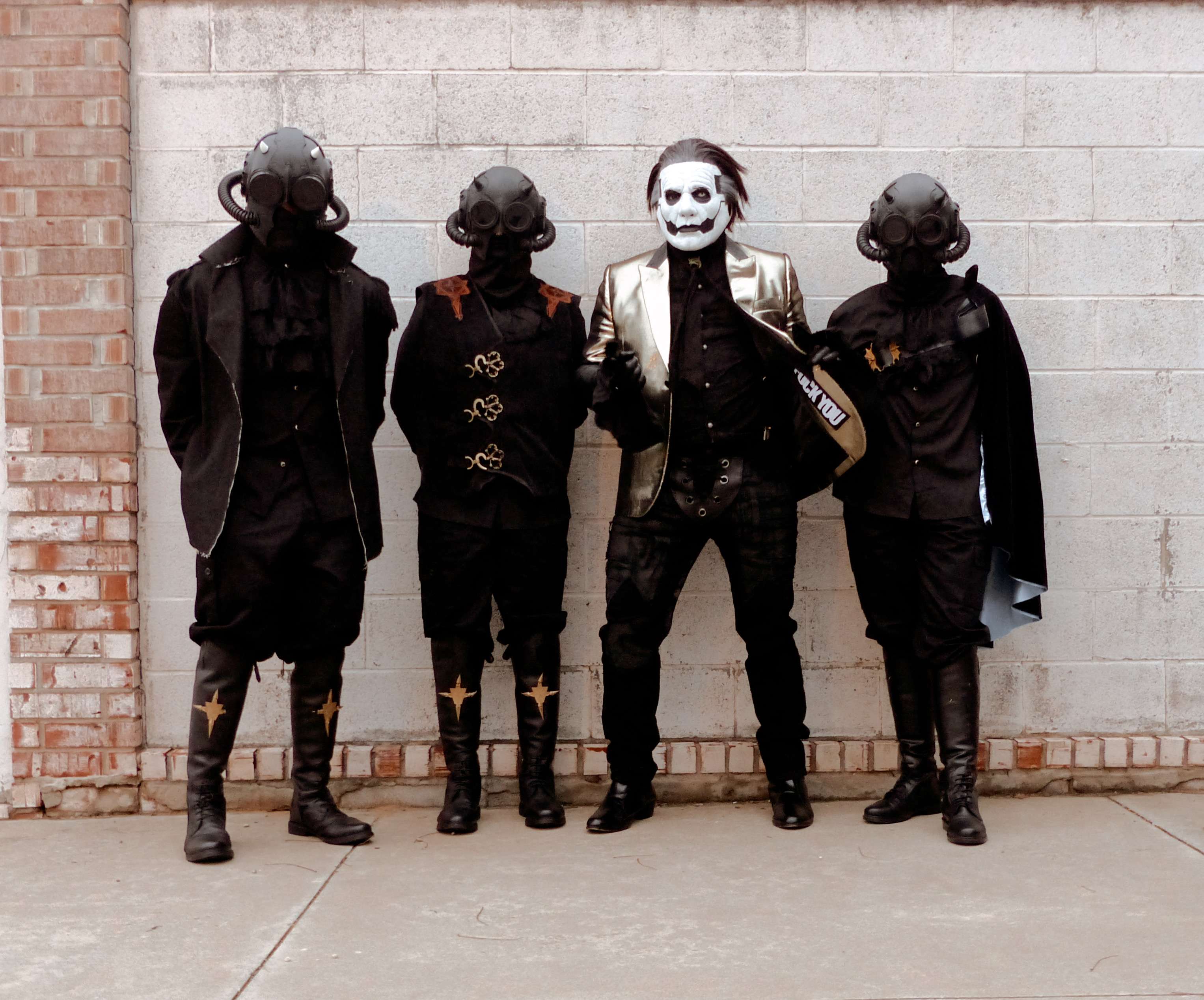 a group of men dressed in gothic outfits standing next to a brick wall