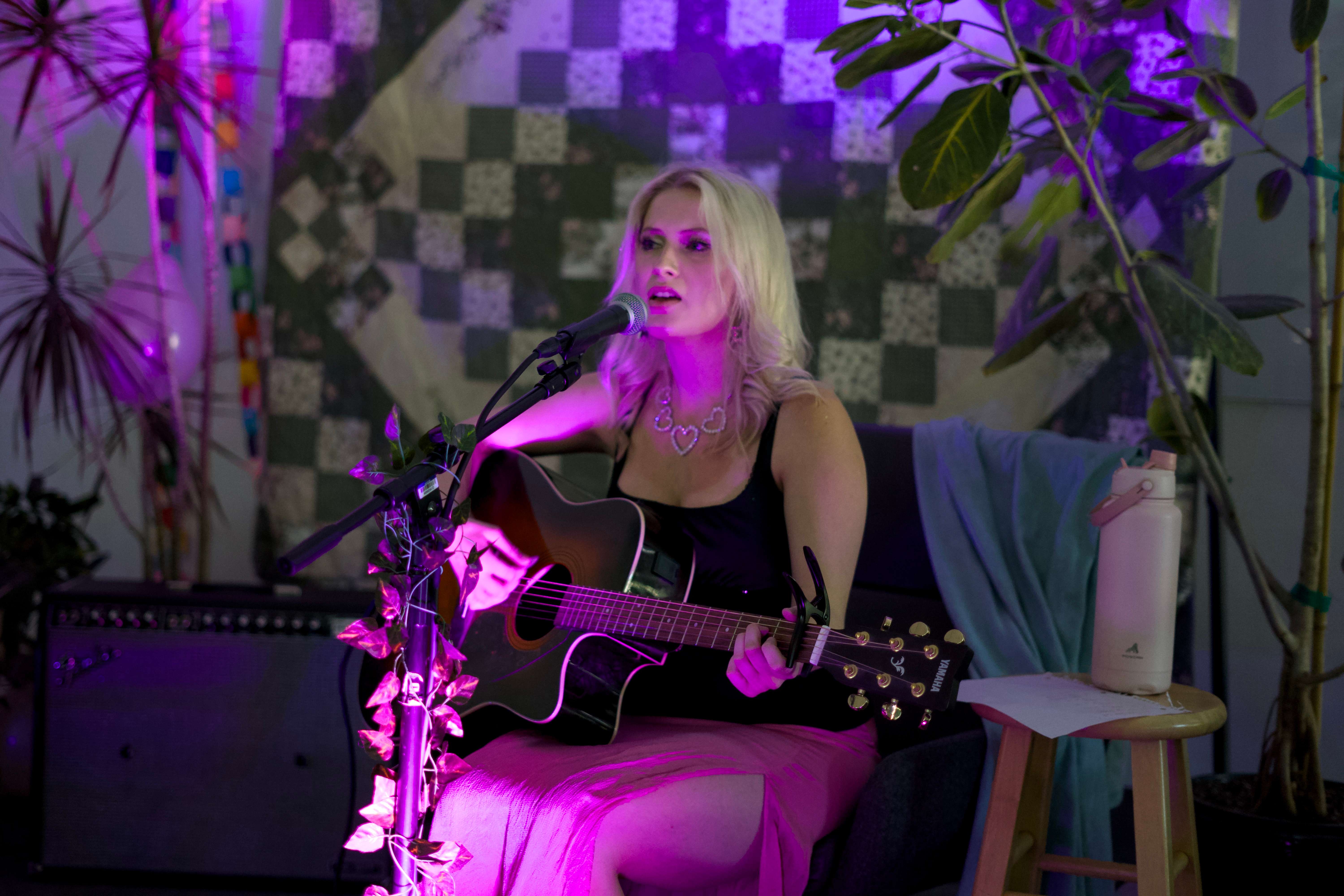 a woman playing an acoustic guitar in front of a purple background