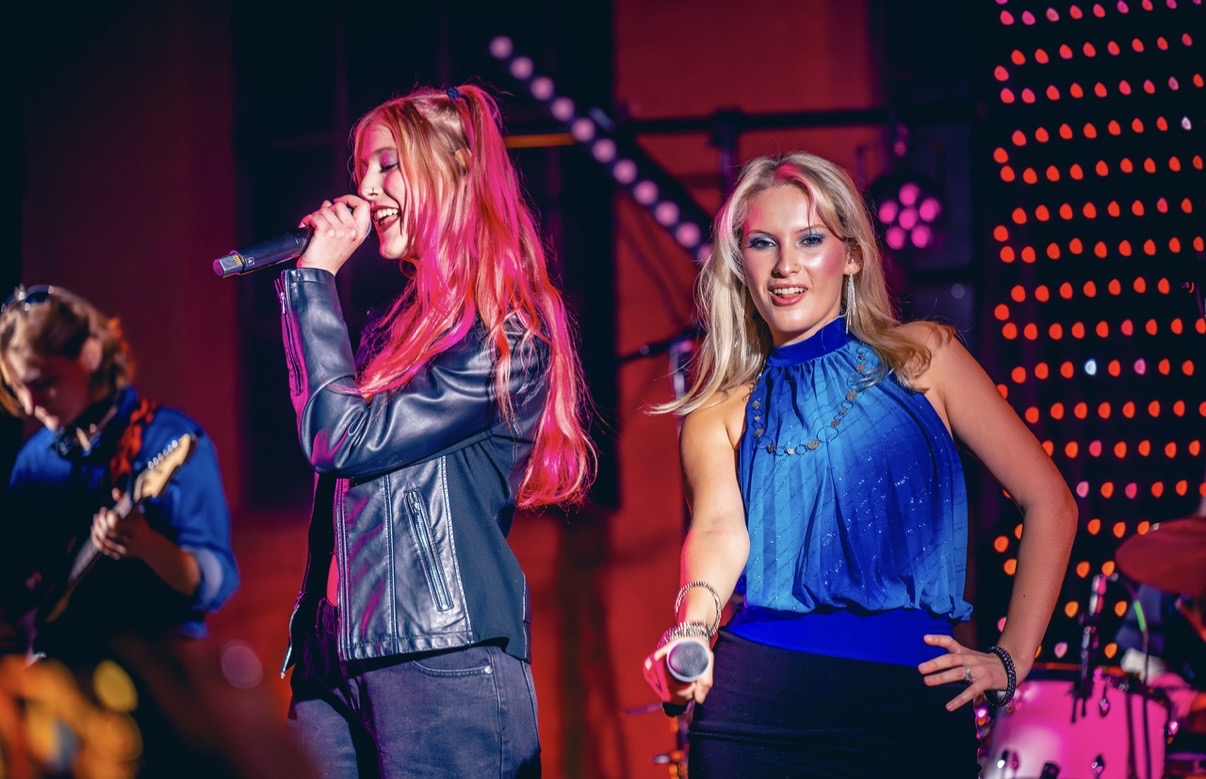 two women with pink hair singing on stage