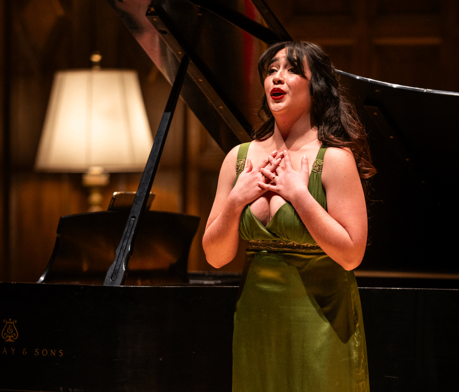 a woman in a green dress standing in front of a grand piano