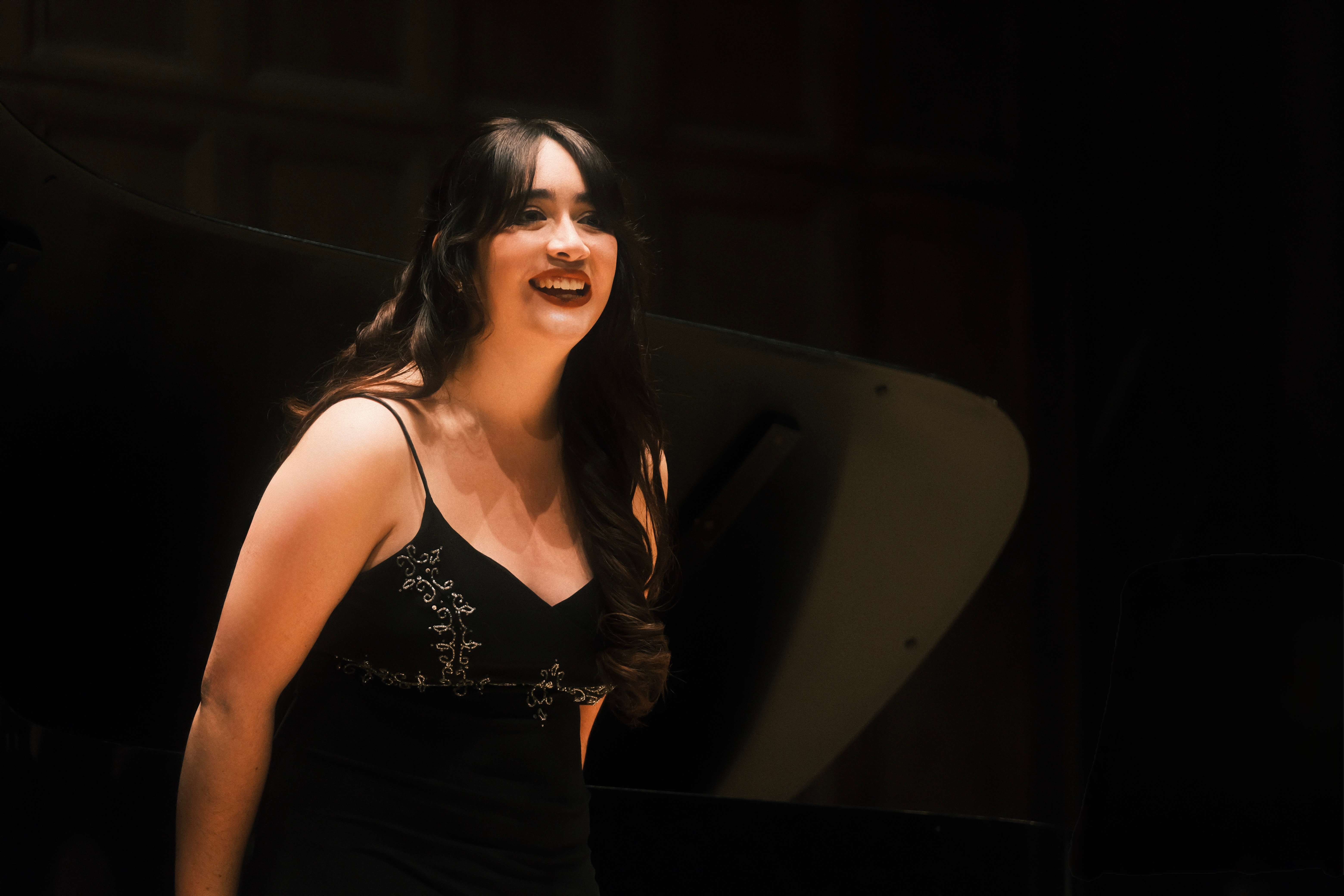 a woman in a black dress smiling in front of a piano