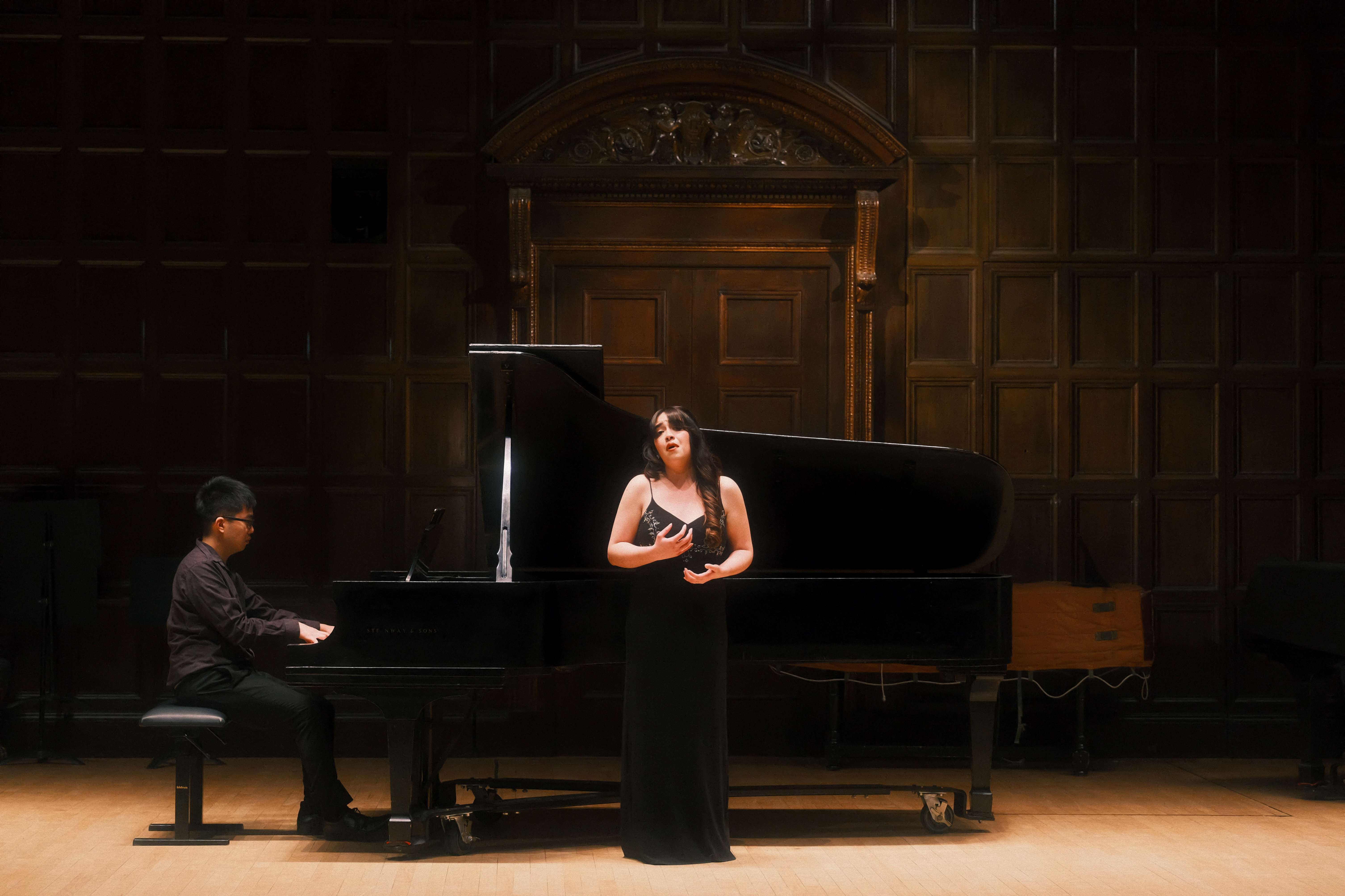 a woman in a black dress standing next to a grand piano