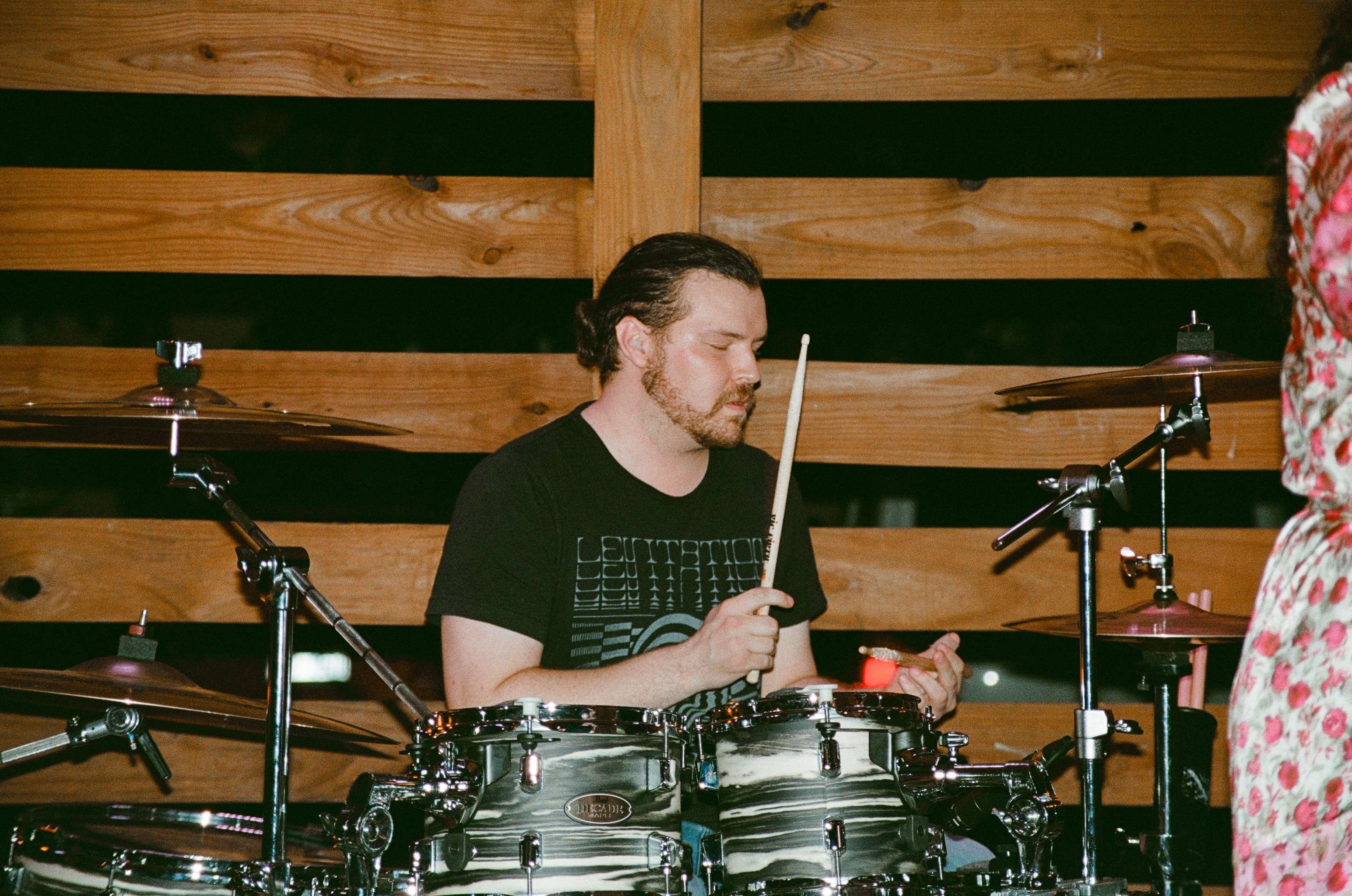 a man playing drums in front of a wooden wall