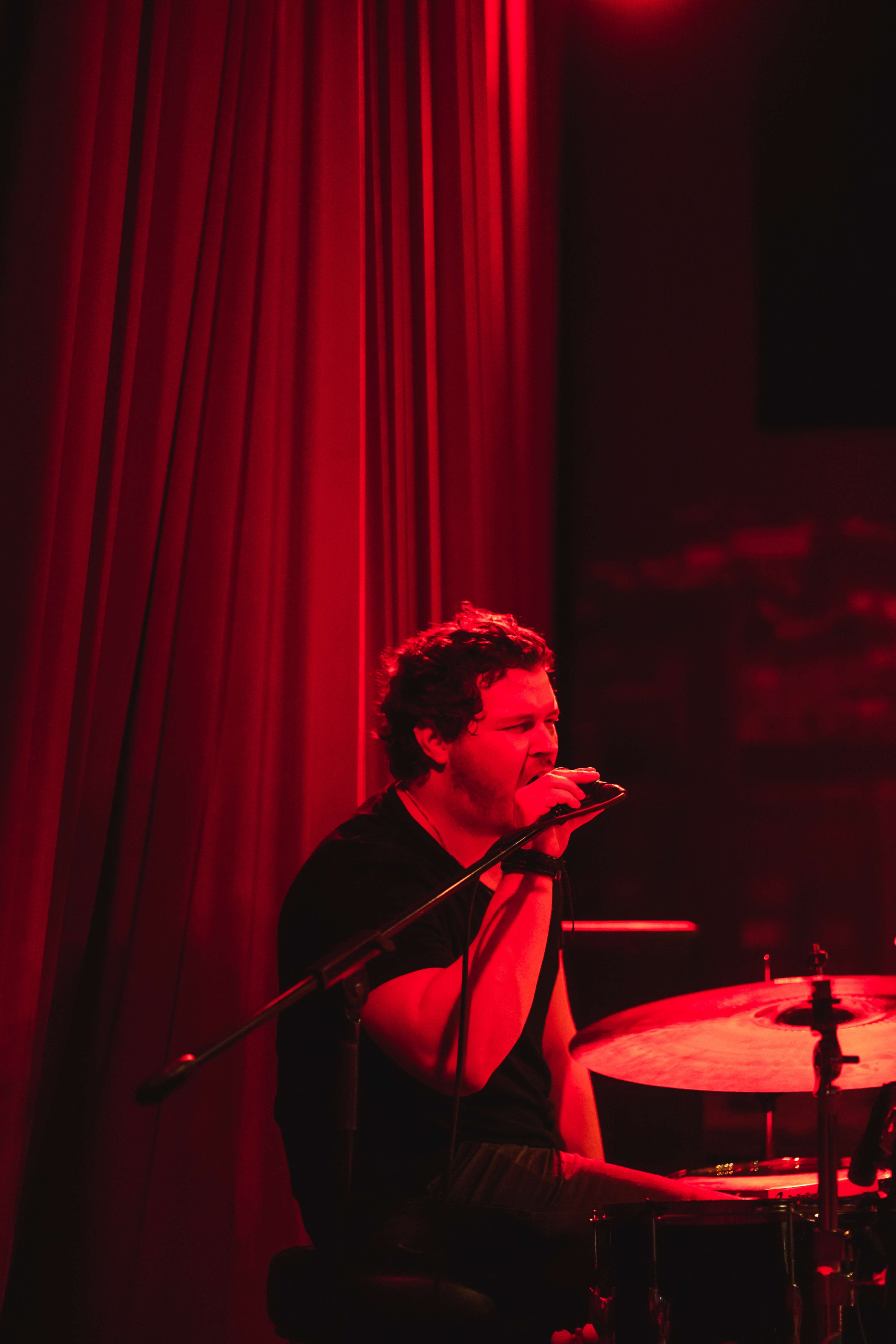 a man playing drums in front of a red curtain