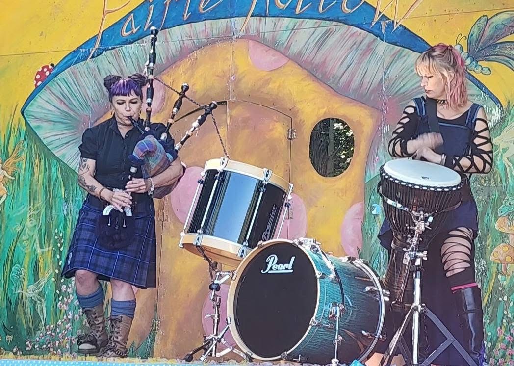 two women in kilts playing drums in front of a mural