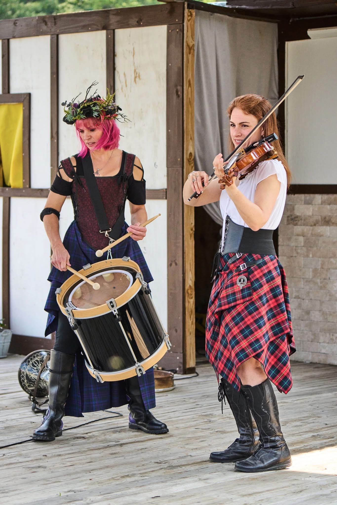 two women in kilts playing a drum on a wooden deck