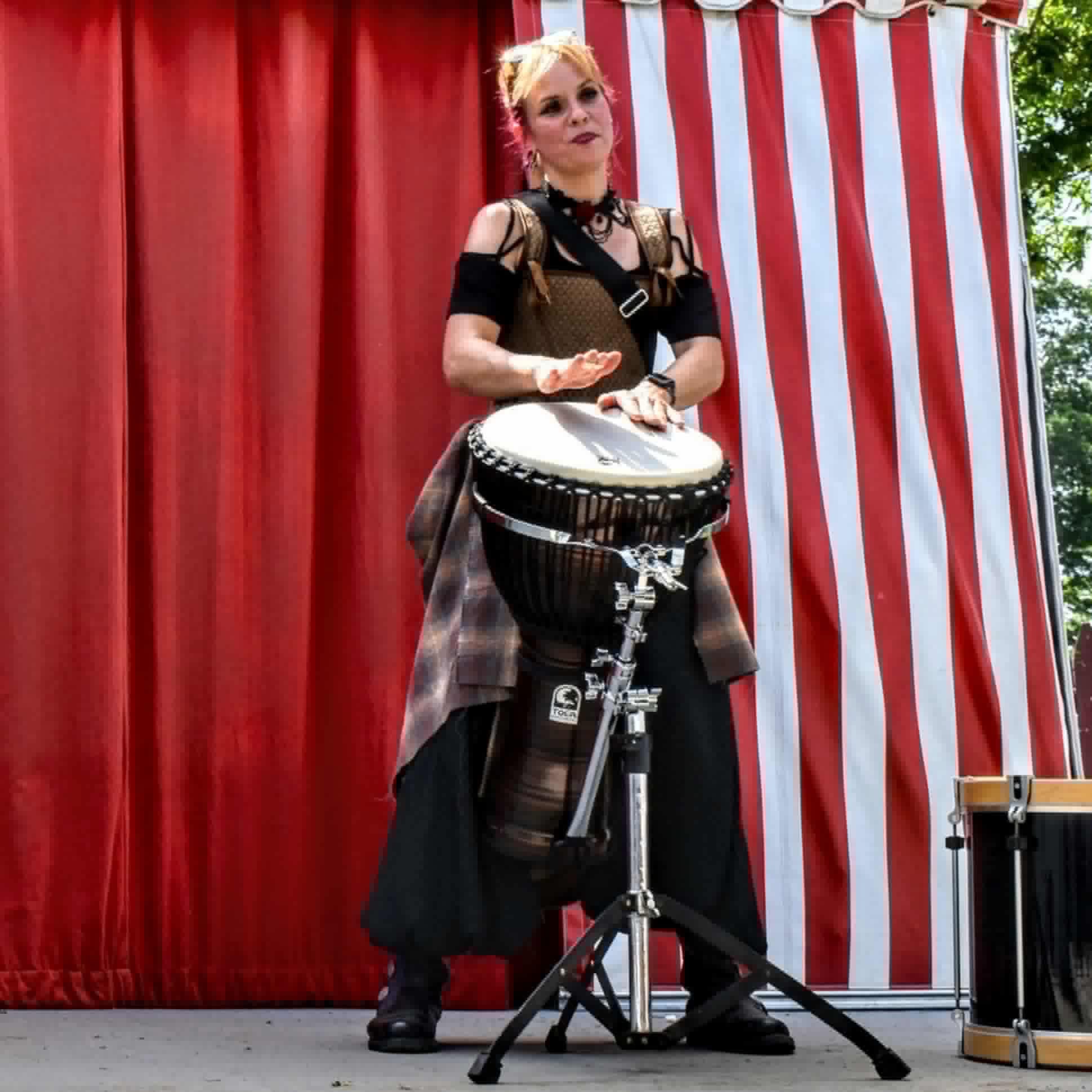 a woman playing a drum in front of a red tent