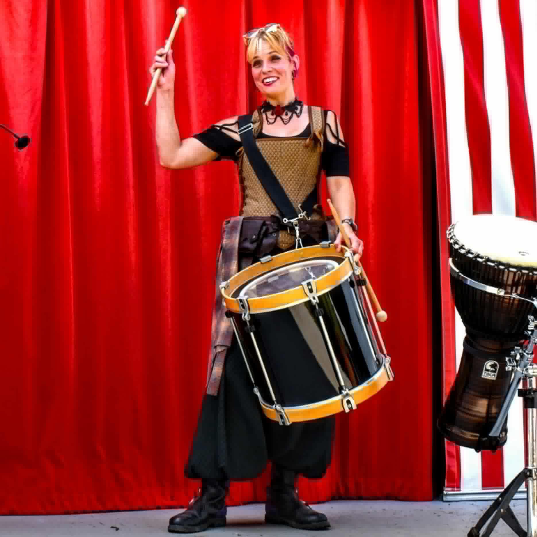 a woman holding a drum in front of a red curtain