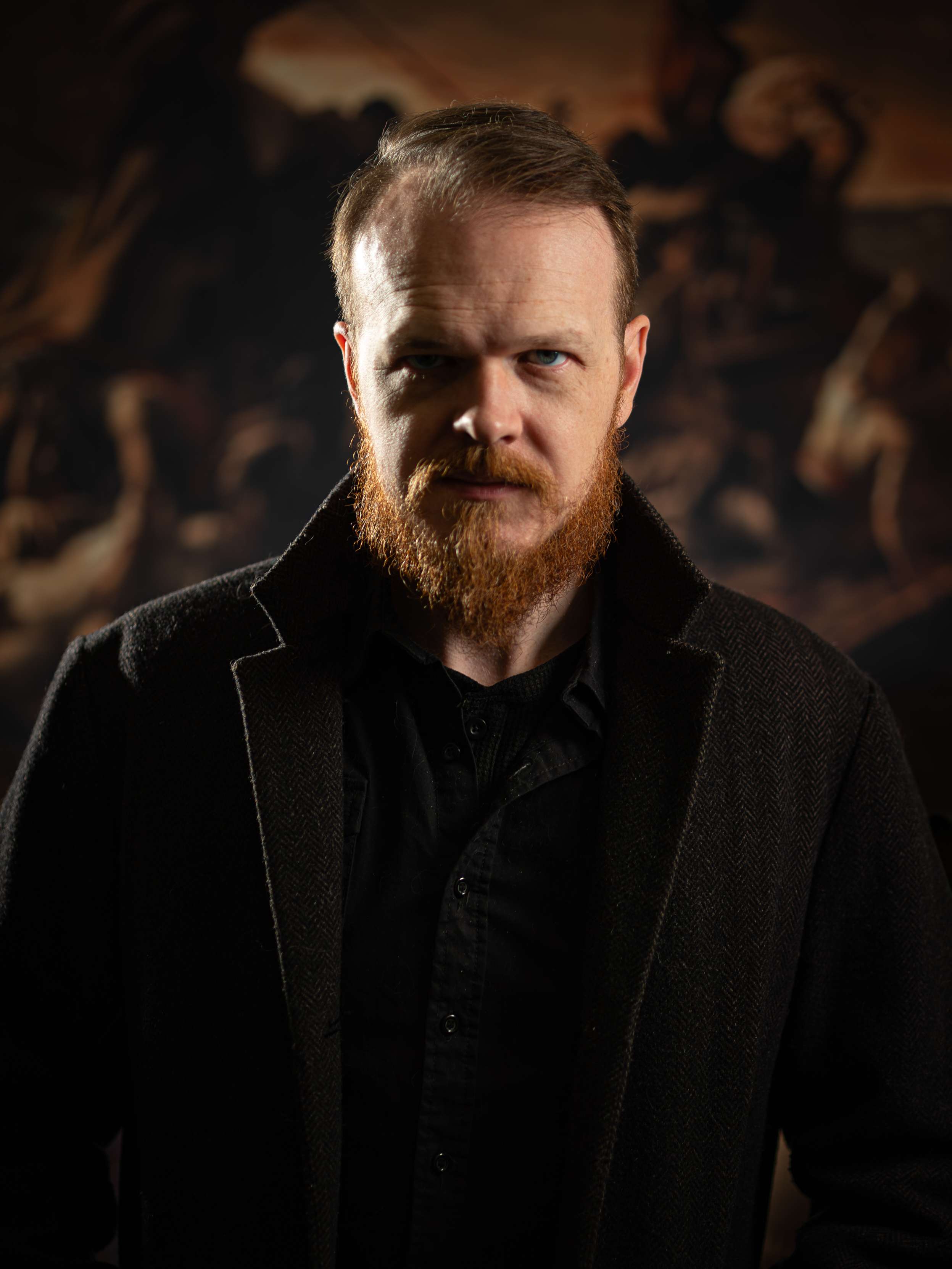 a man with a red beard standing in front of a painting