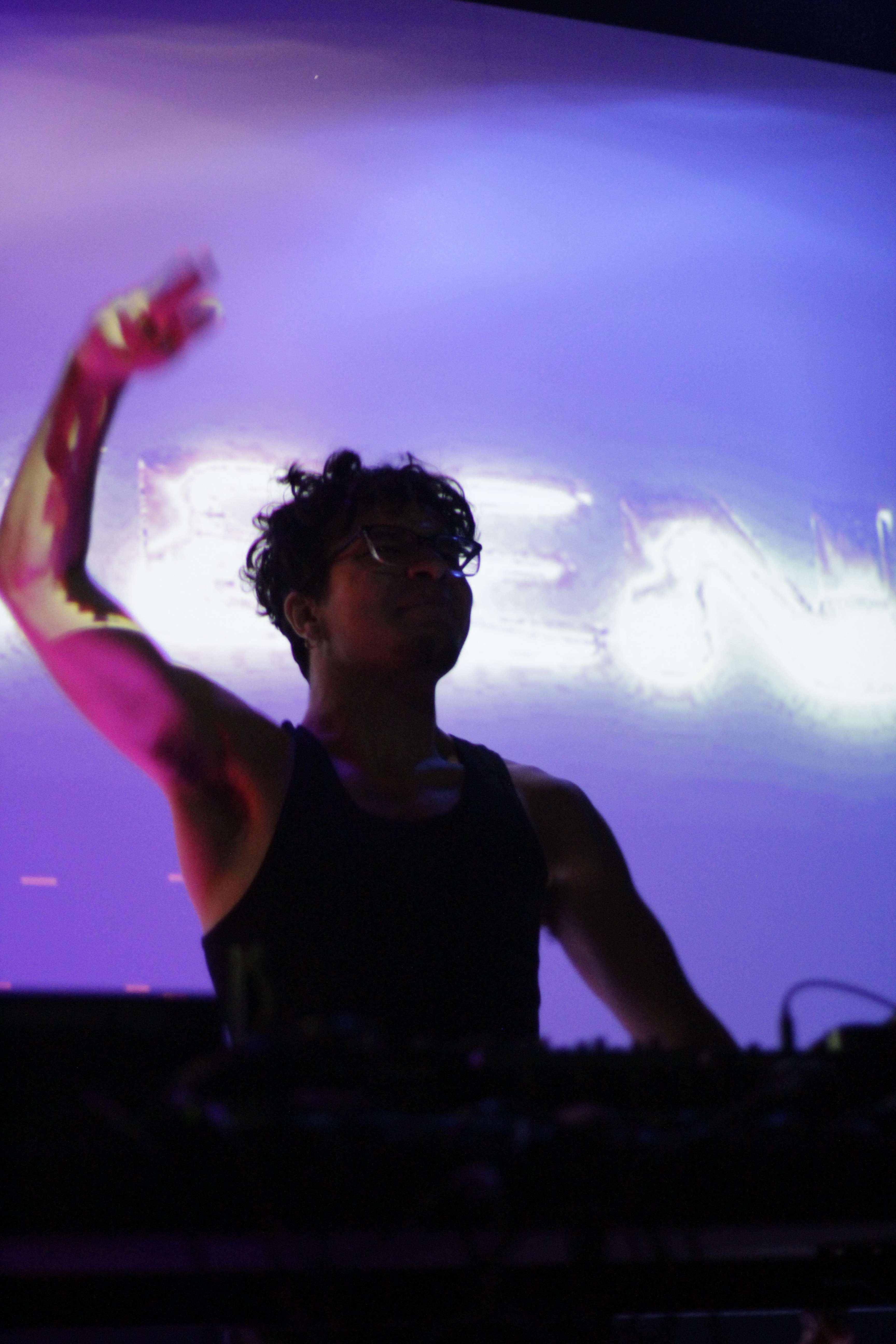 a dj with his hands up in front of a screen