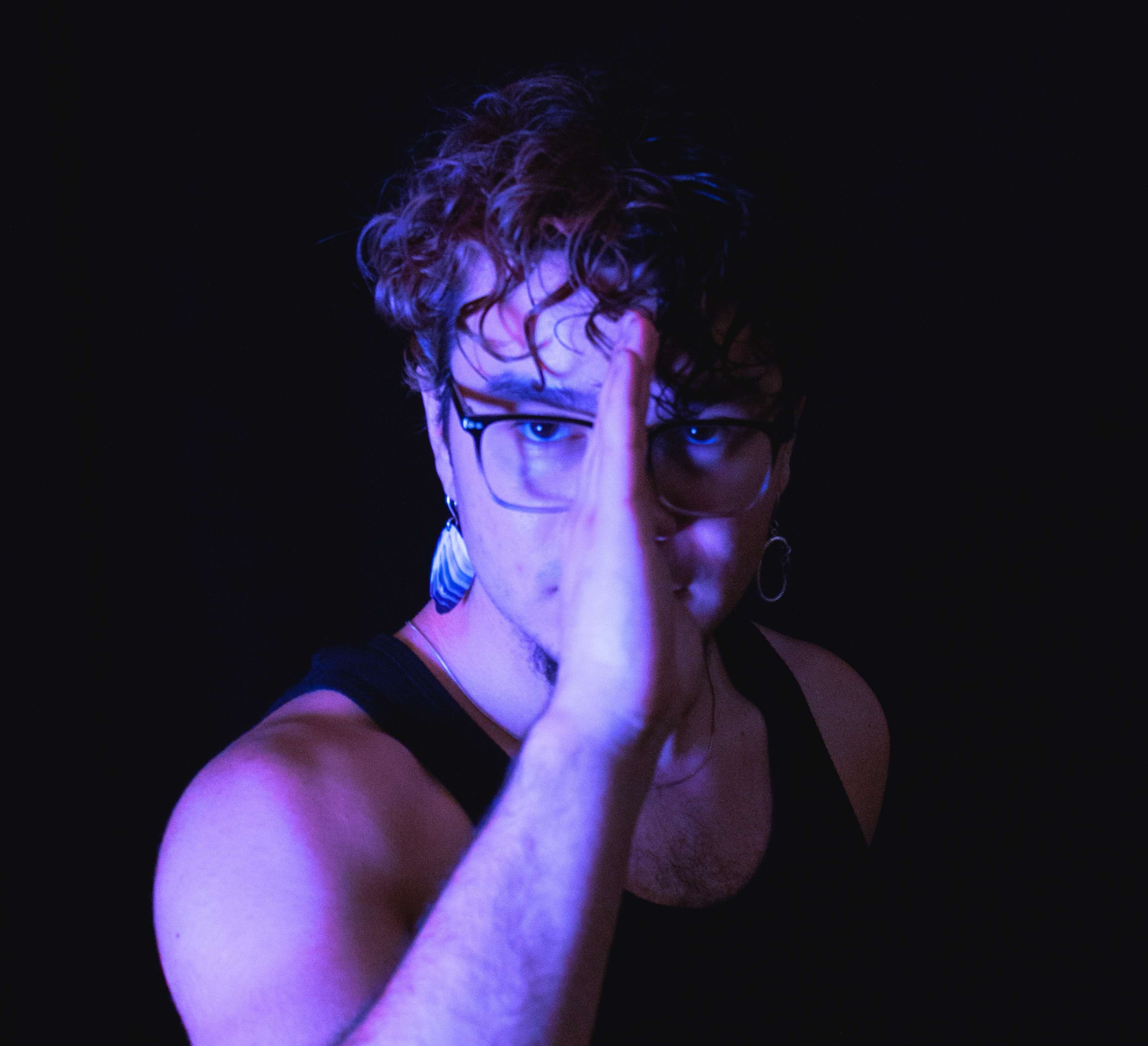 a man with glasses is holding his hand up in front of a dark background