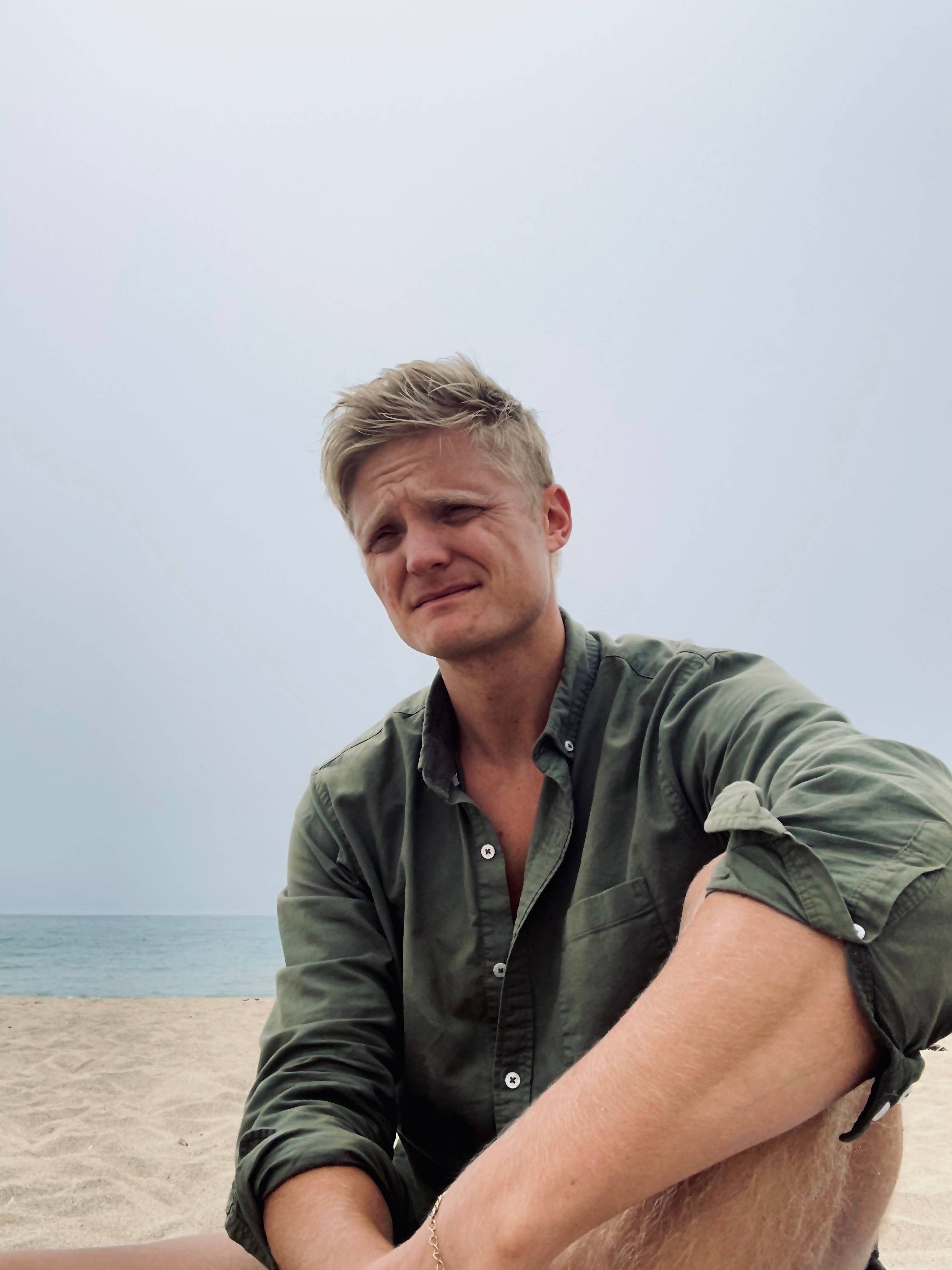 a young man sitting on the beach with his feet on the sand
