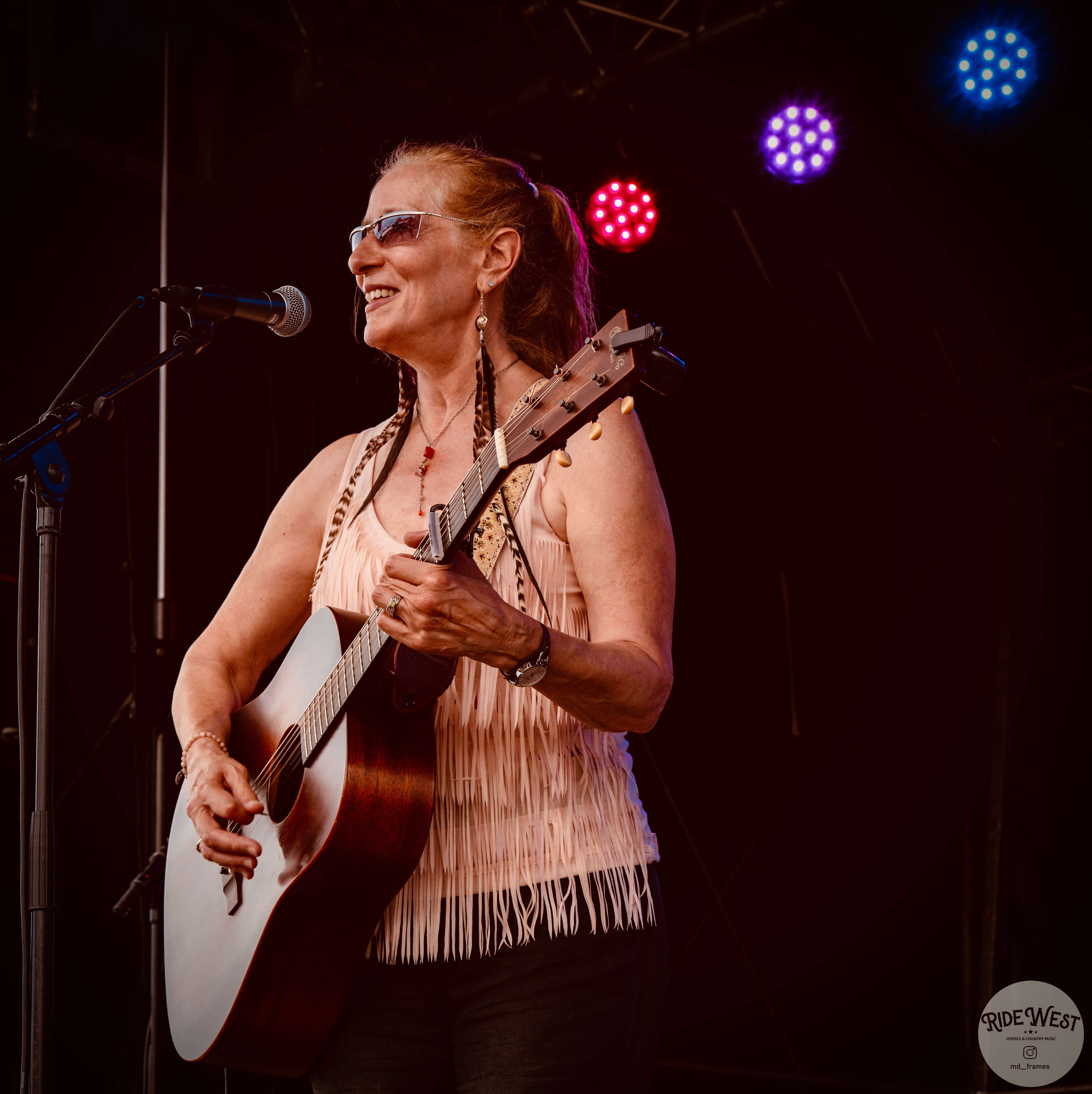 a woman singing into a microphone with an acoustic guitar