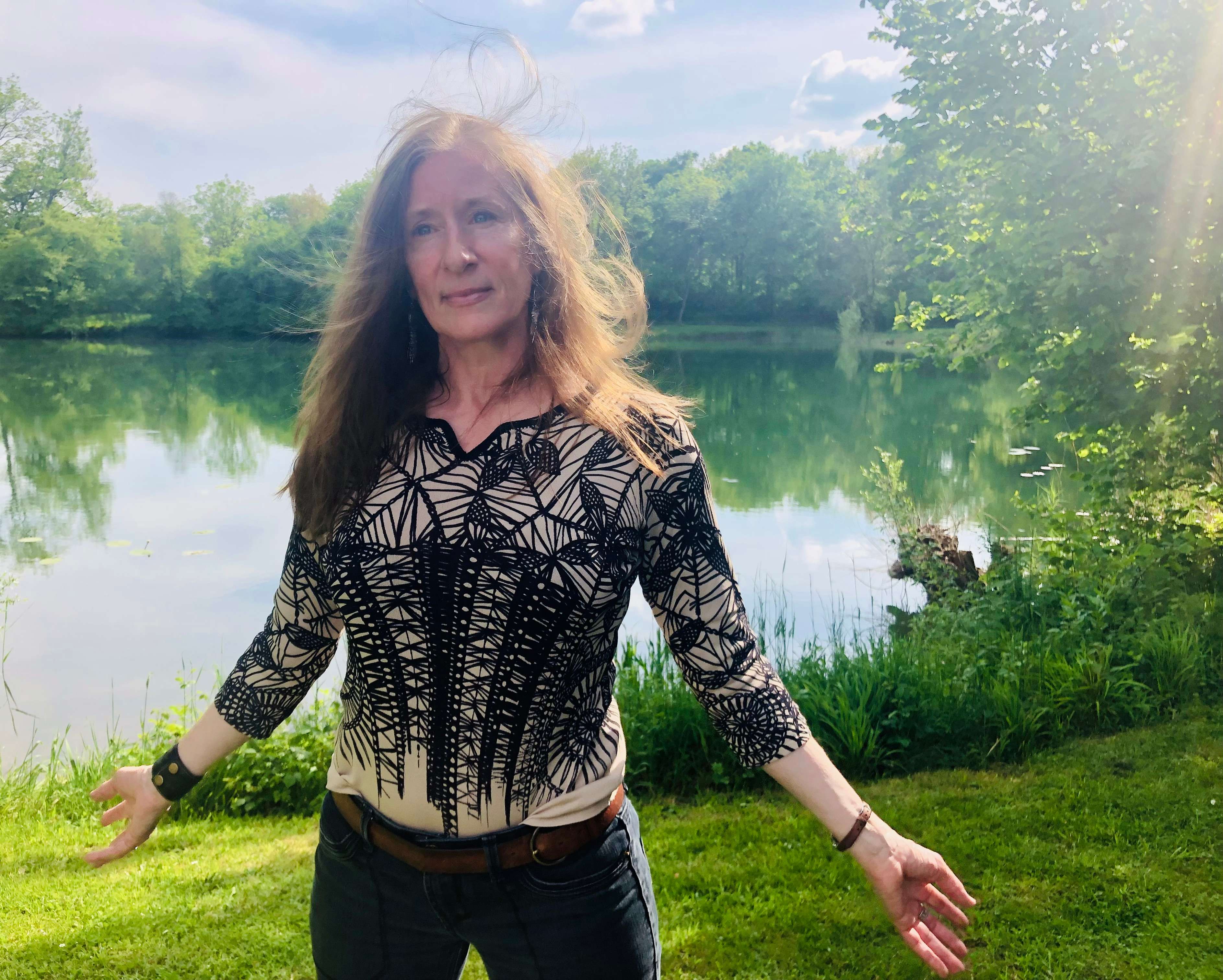 a woman standing in front of a lake with her arms outstretched