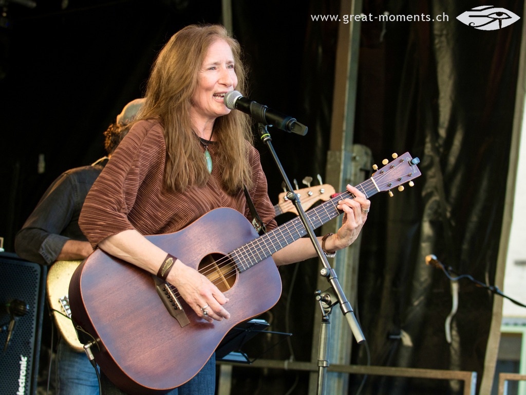 a woman singing into a microphone while holding an acoustic guitar