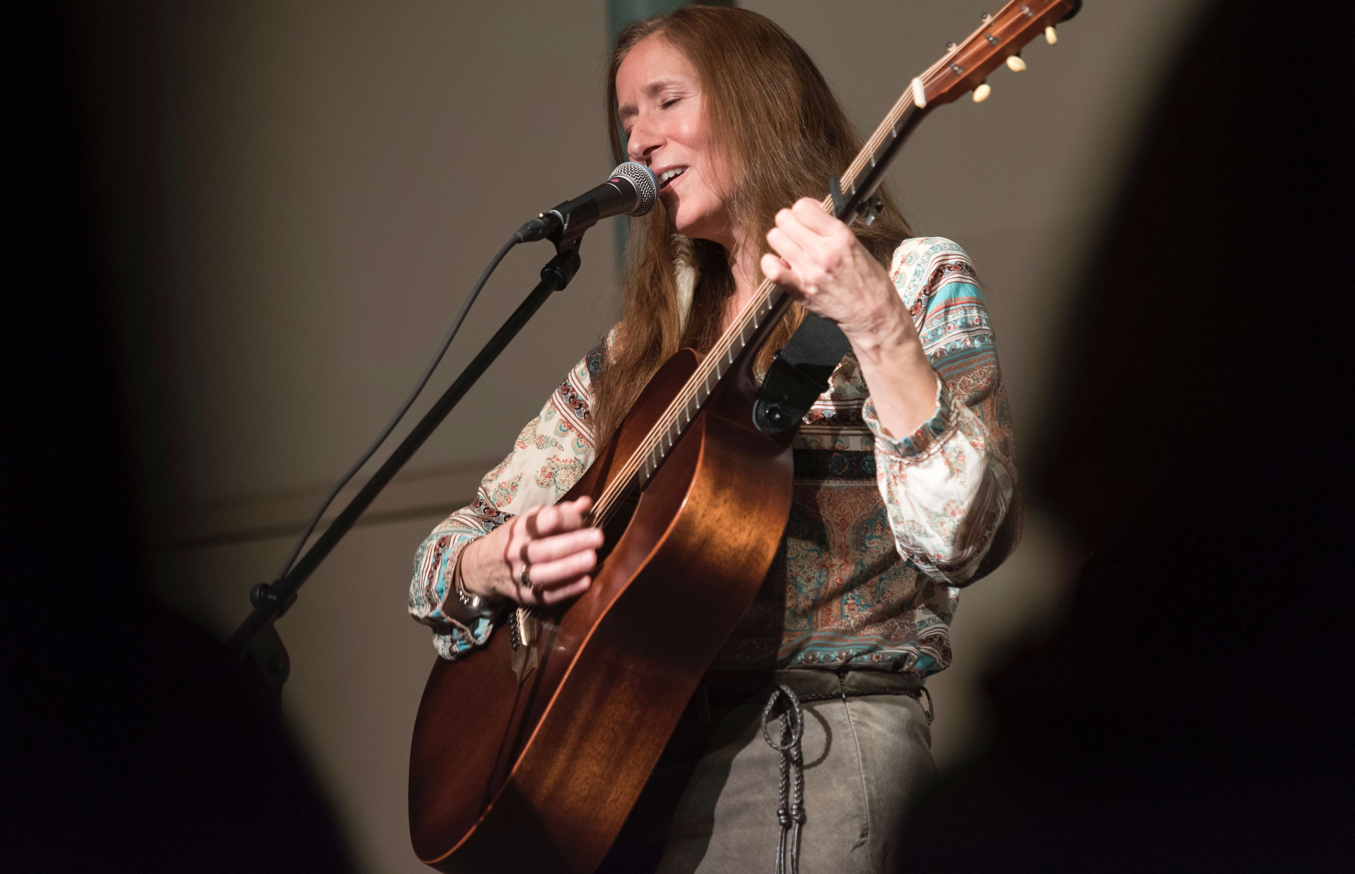 a woman singing into a microphone while playing an acoustic guitar