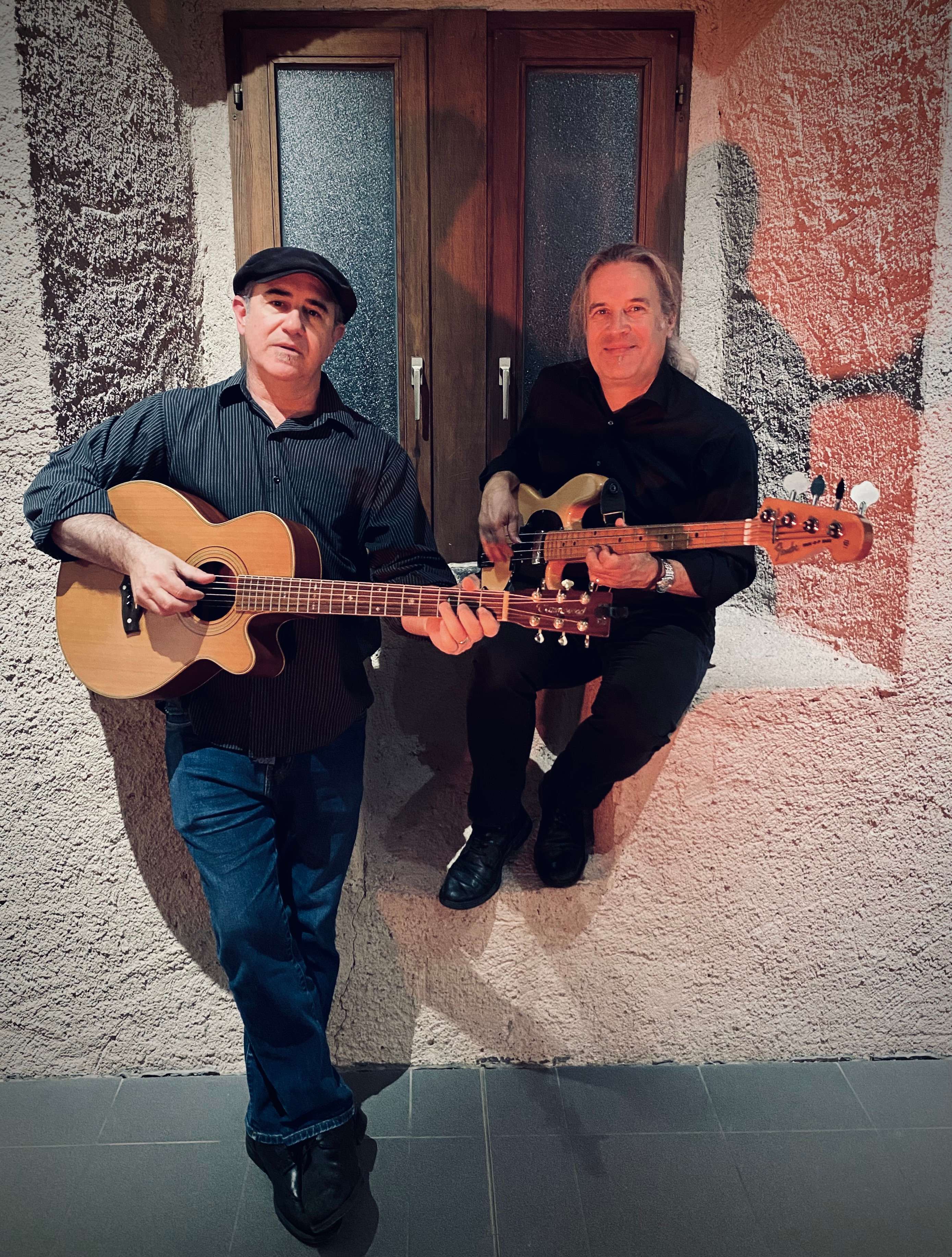 two men playing guitars in front of a window