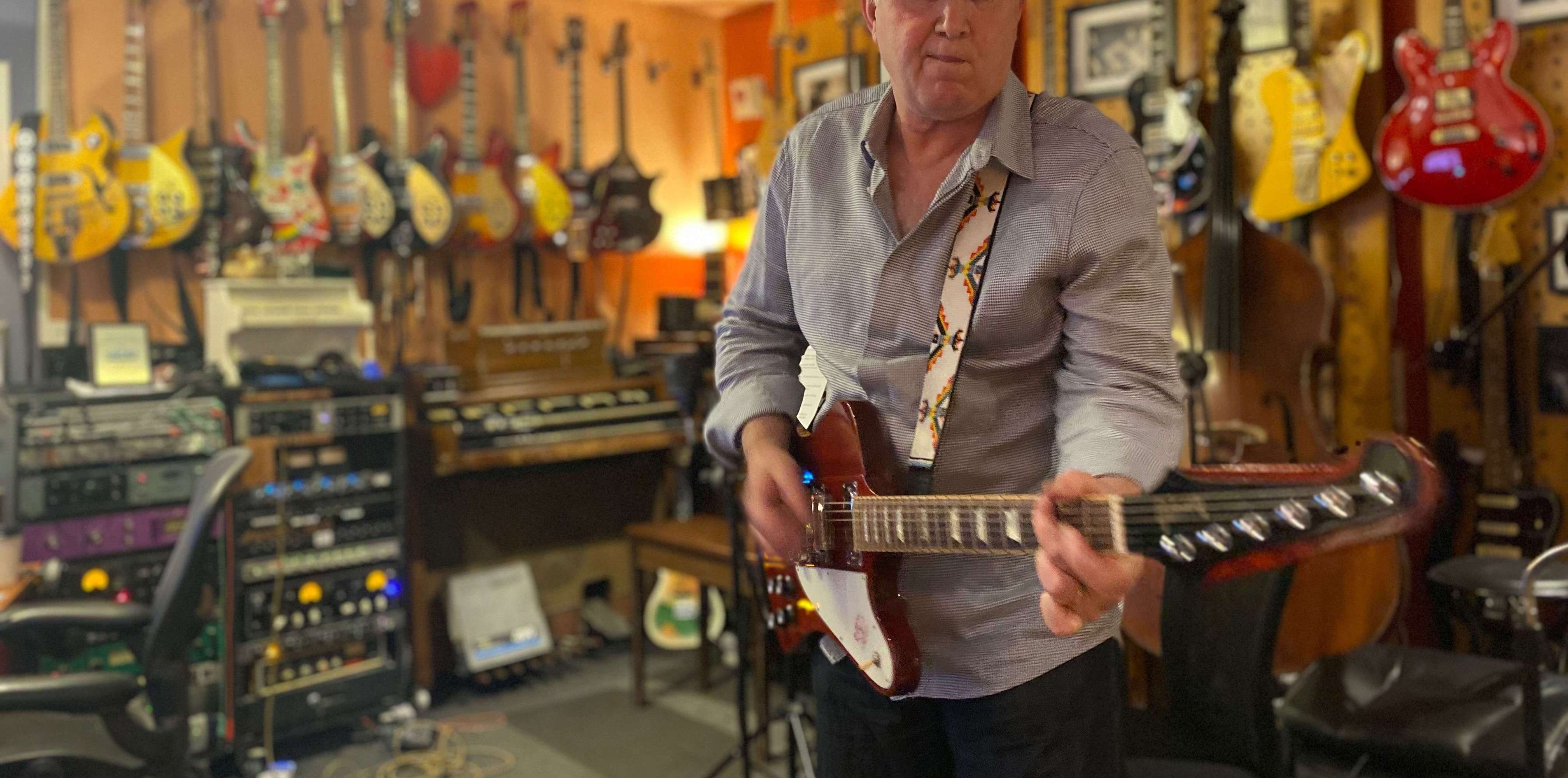 a man playing an electric guitar in a room full of guitars