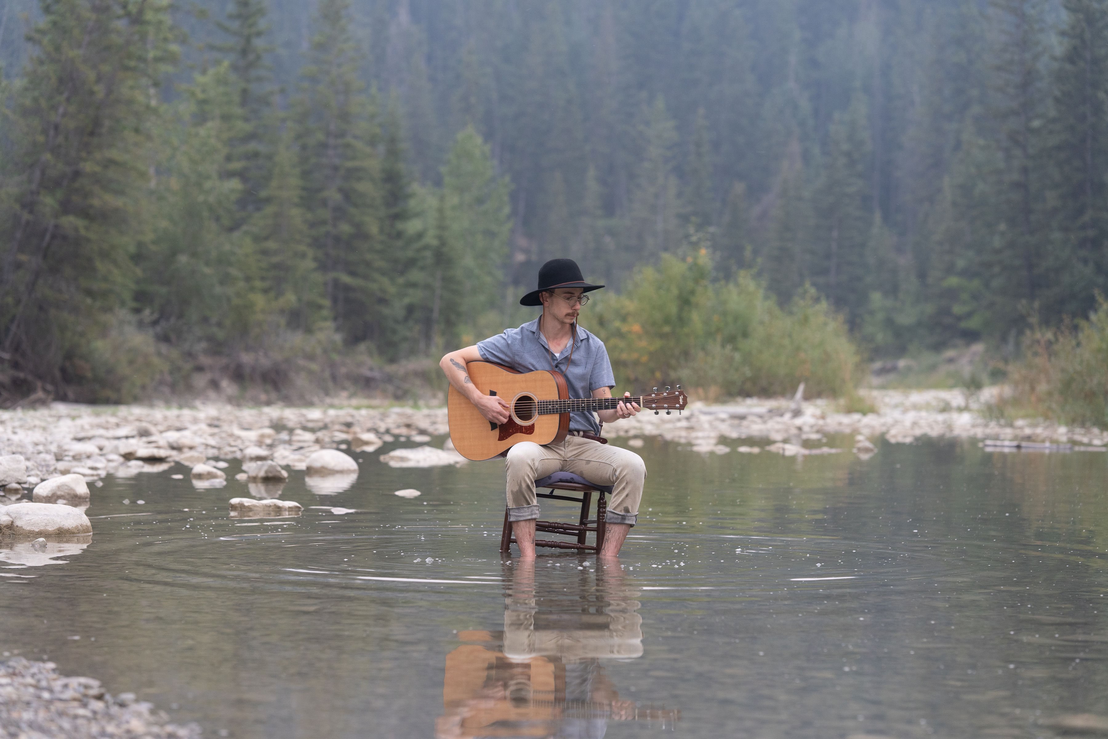 a man sitting in a chair playing an acoustic guitar in a river
