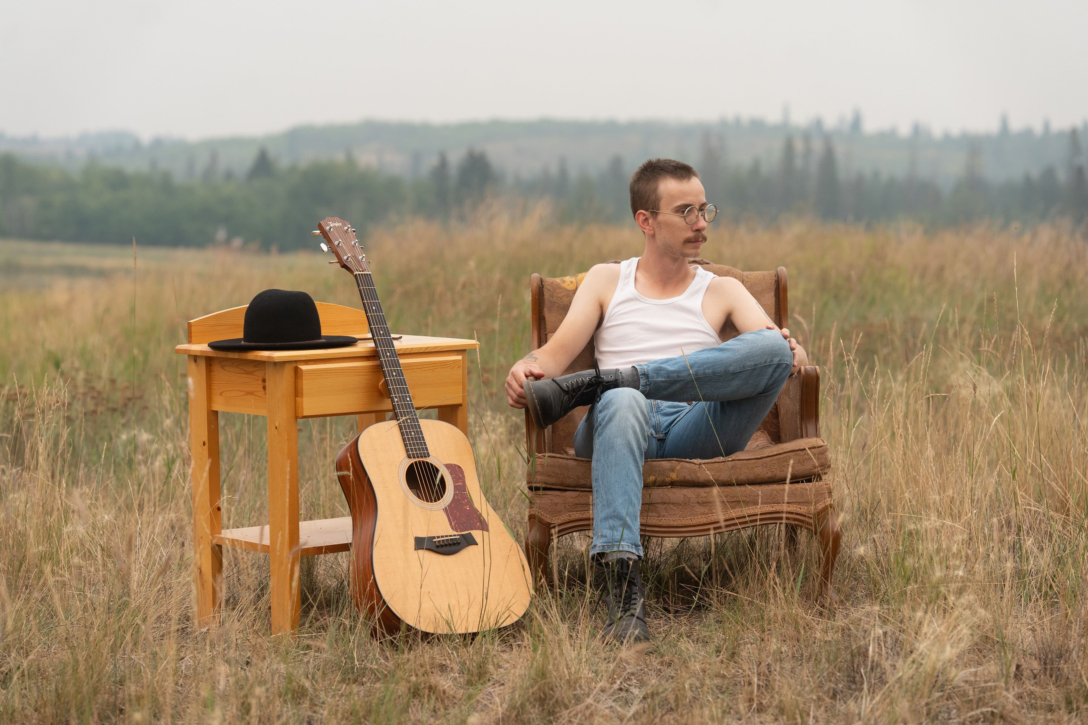 a man sitting on a chair in a field with an acoustic guitar