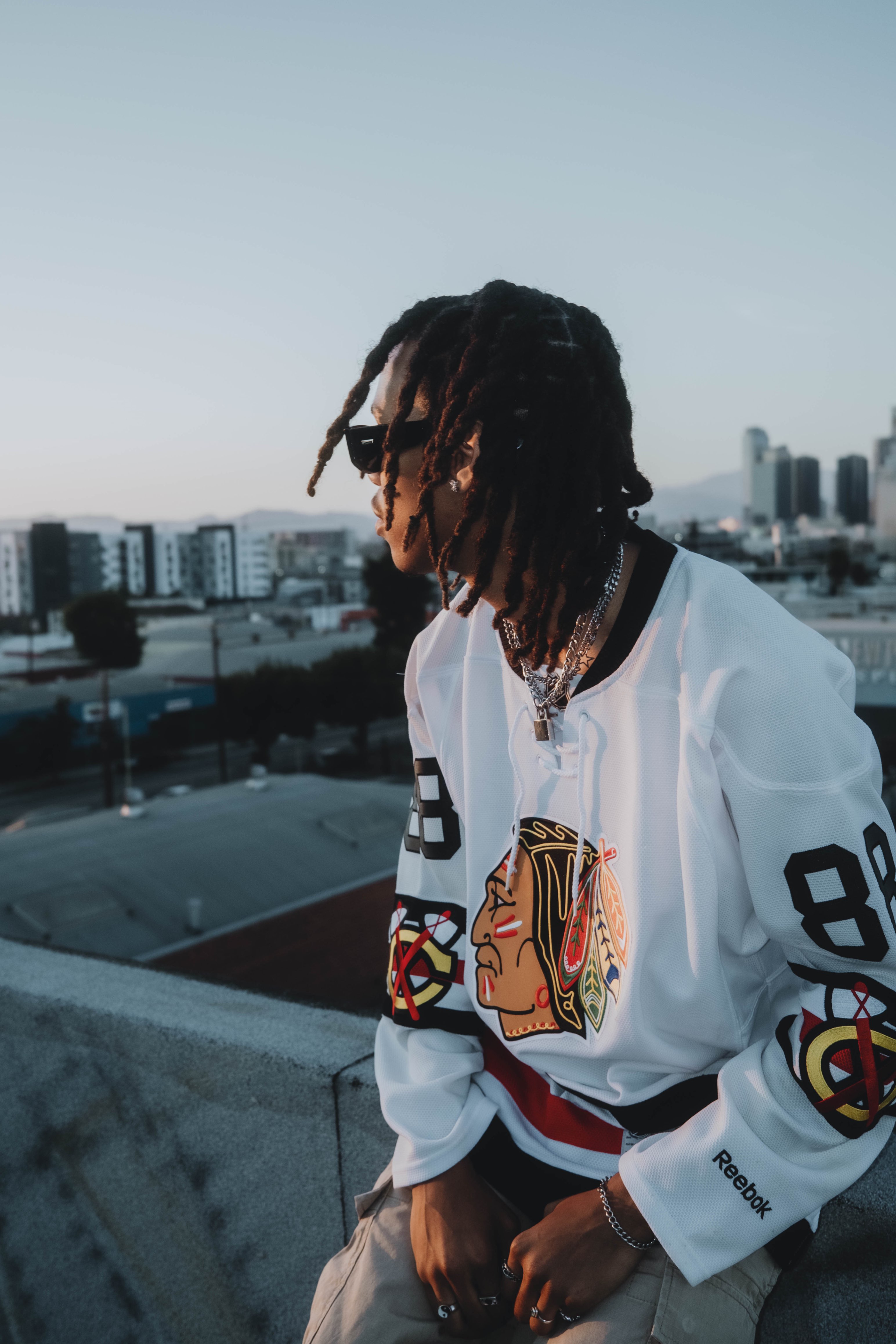 a man with dreadlocks sitting on a ledge with a chicago blackhawks jersey