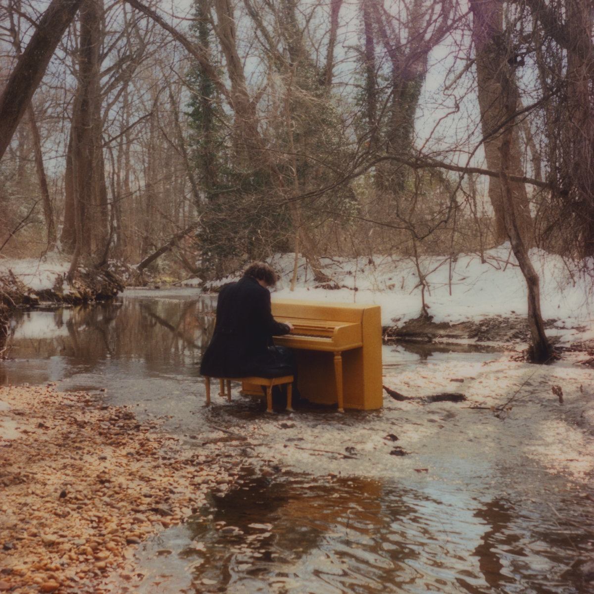 a man sitting on a yellow piano in a wooded area