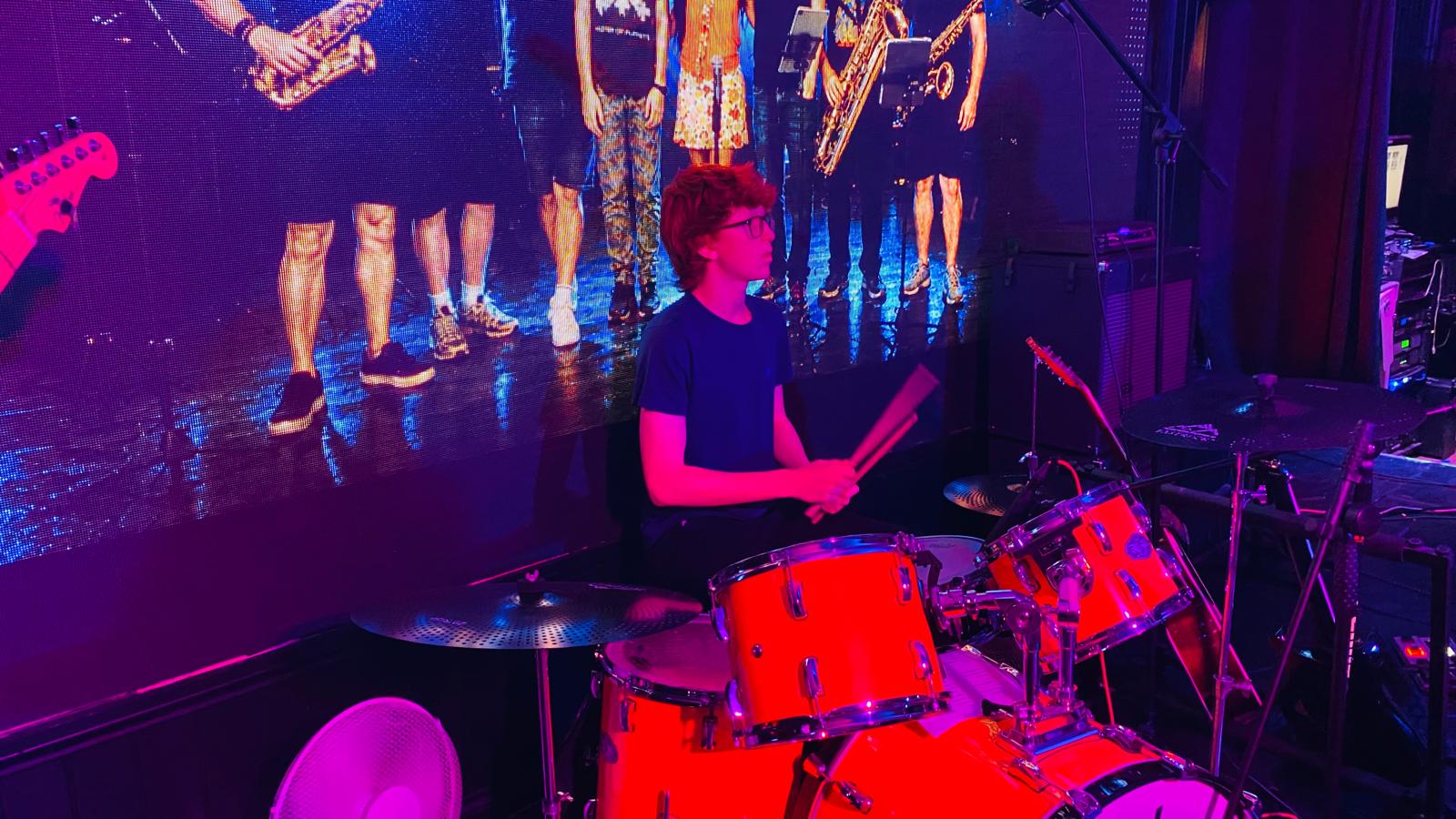 a group of people playing drums in front of a large screen