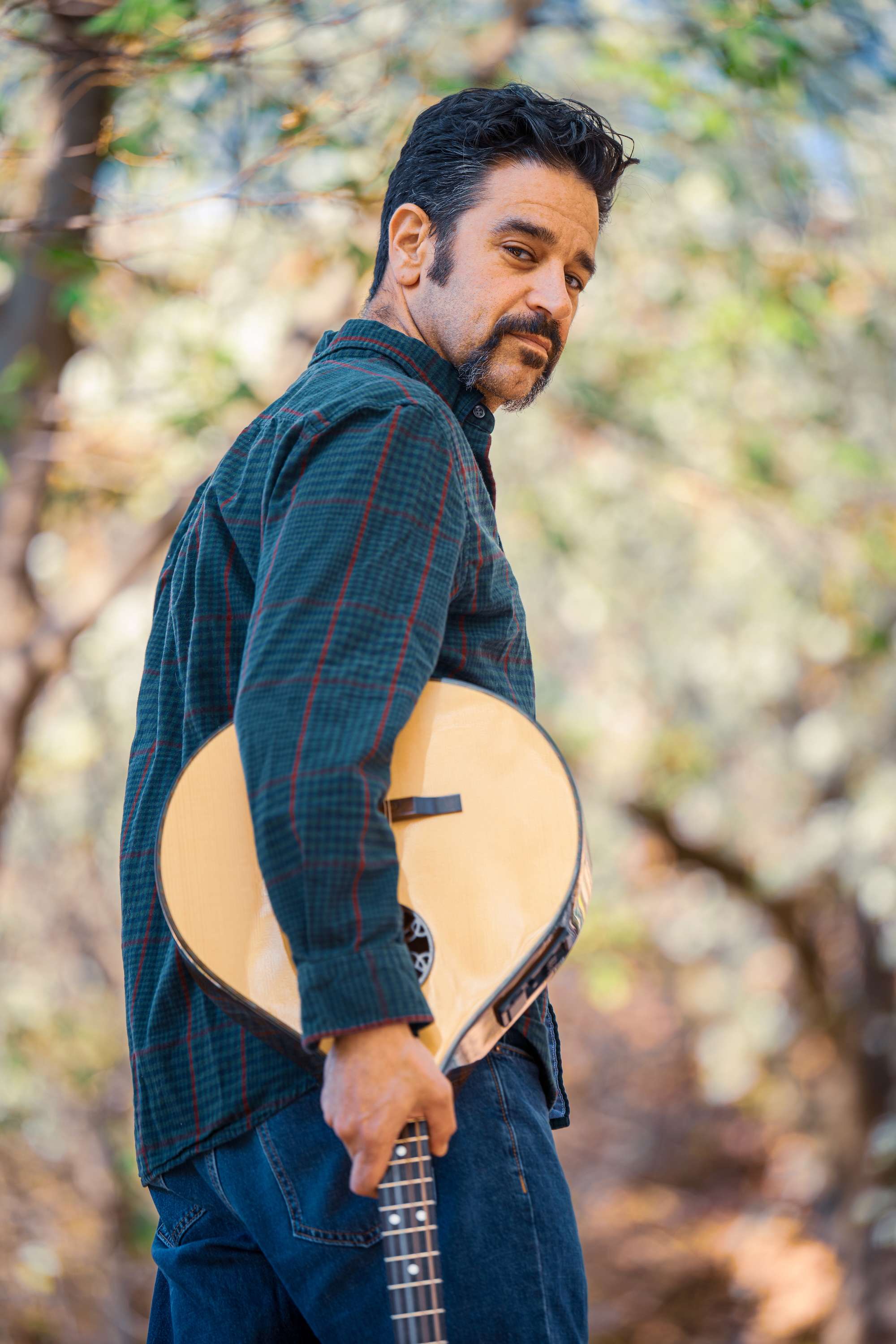 a man holding a guitar in the woods