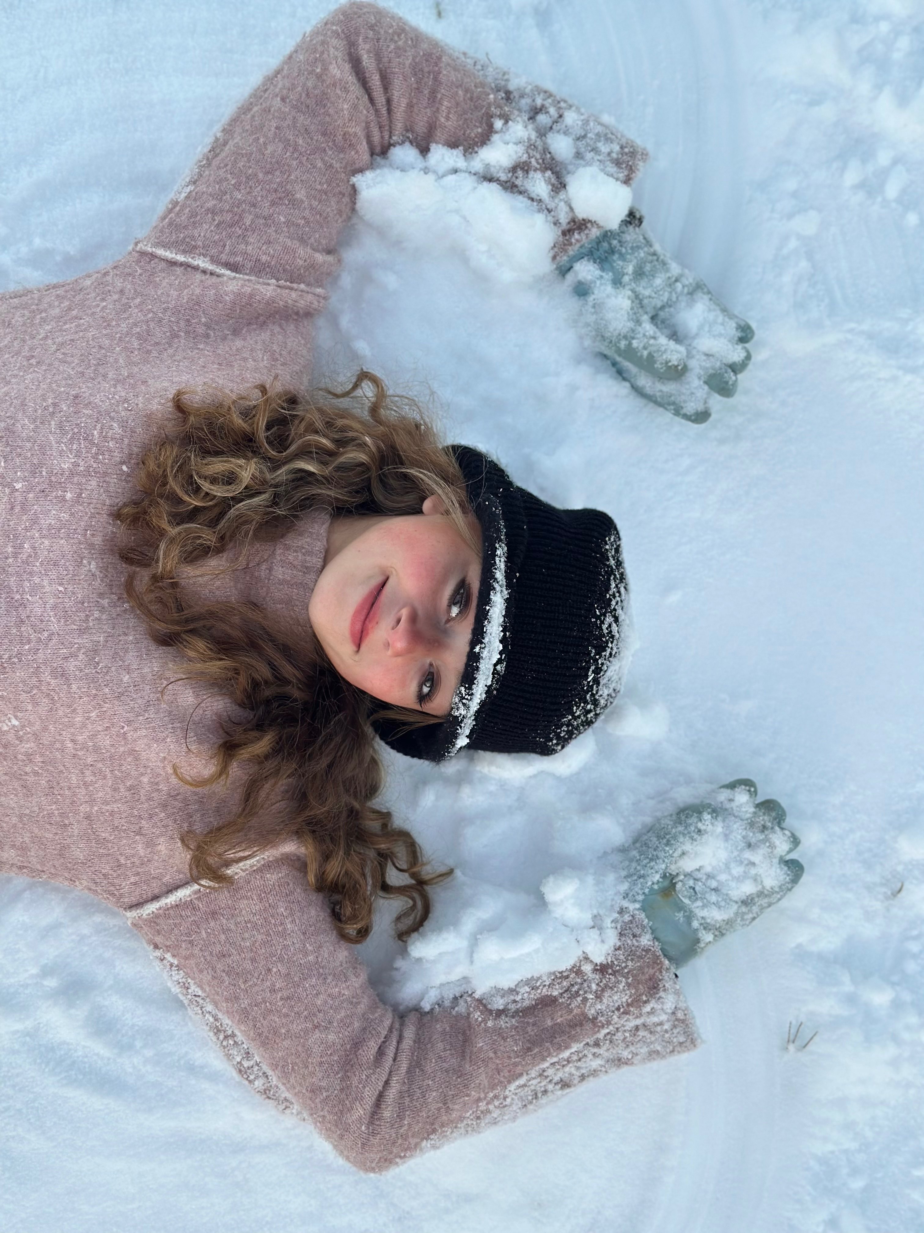 a girl laying in the snow with her hands in the air