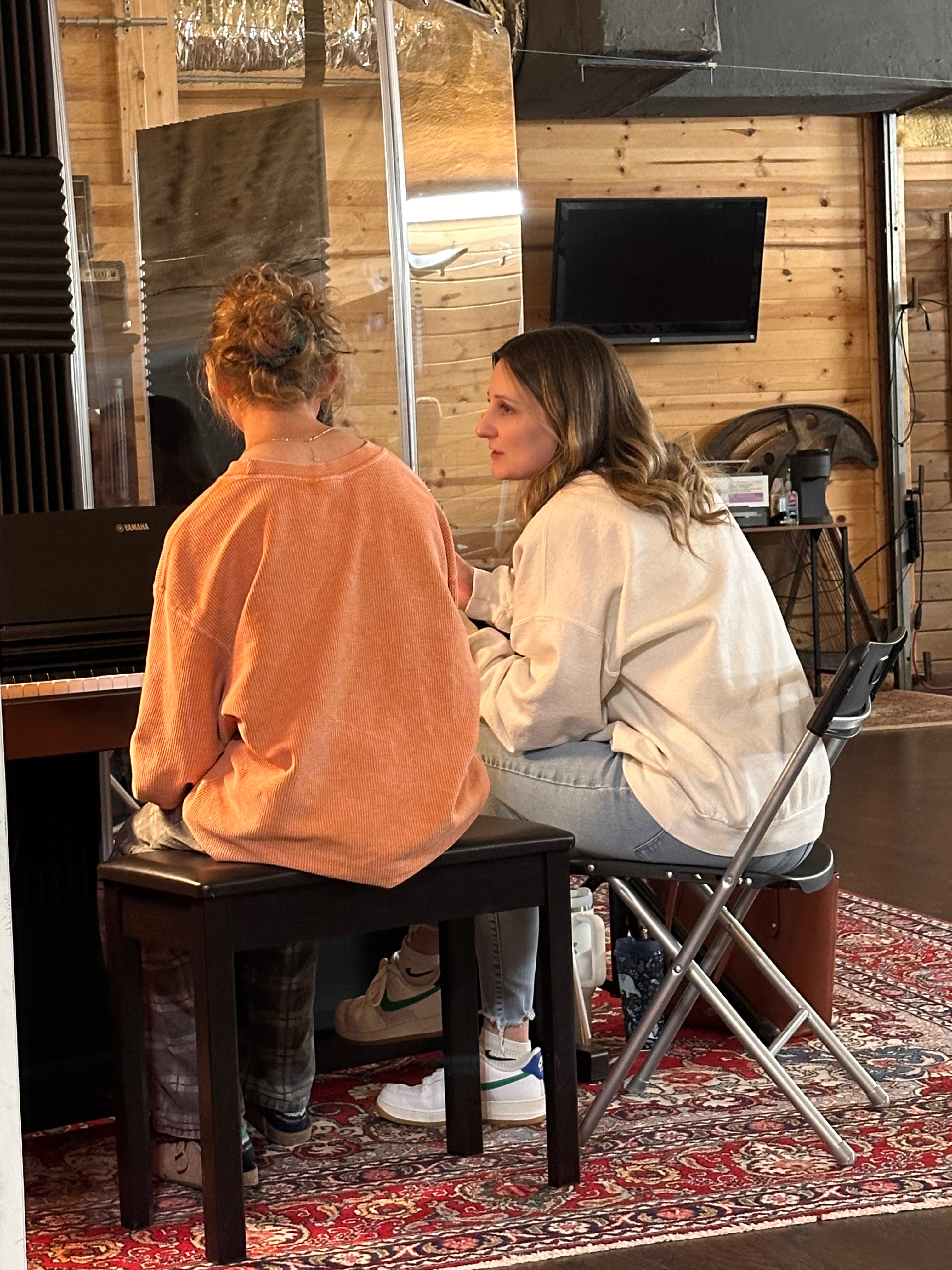 two women sitting at a piano in a recording studio