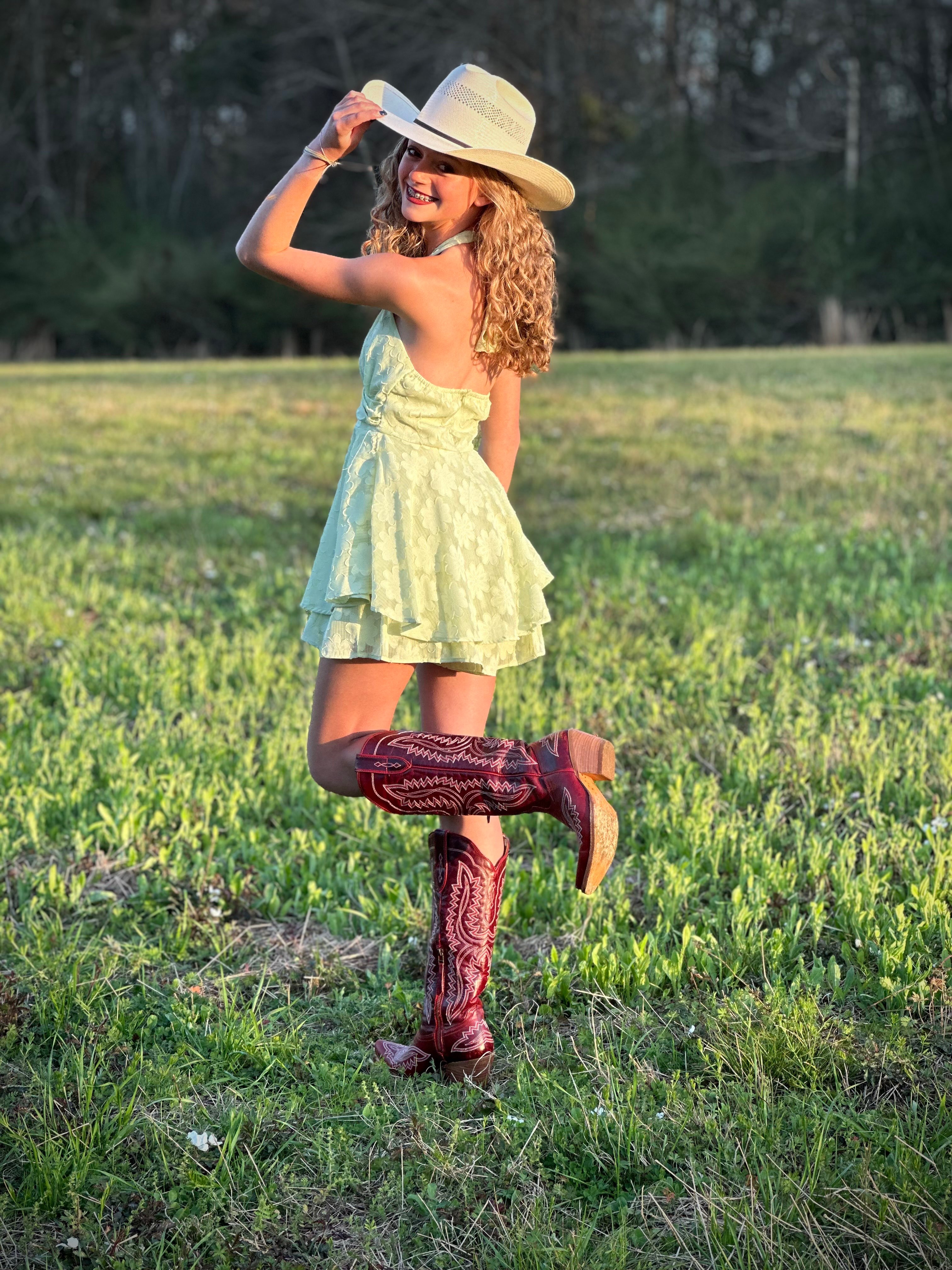 a girl in a cowboy hat and cowboy boots posing in a field
