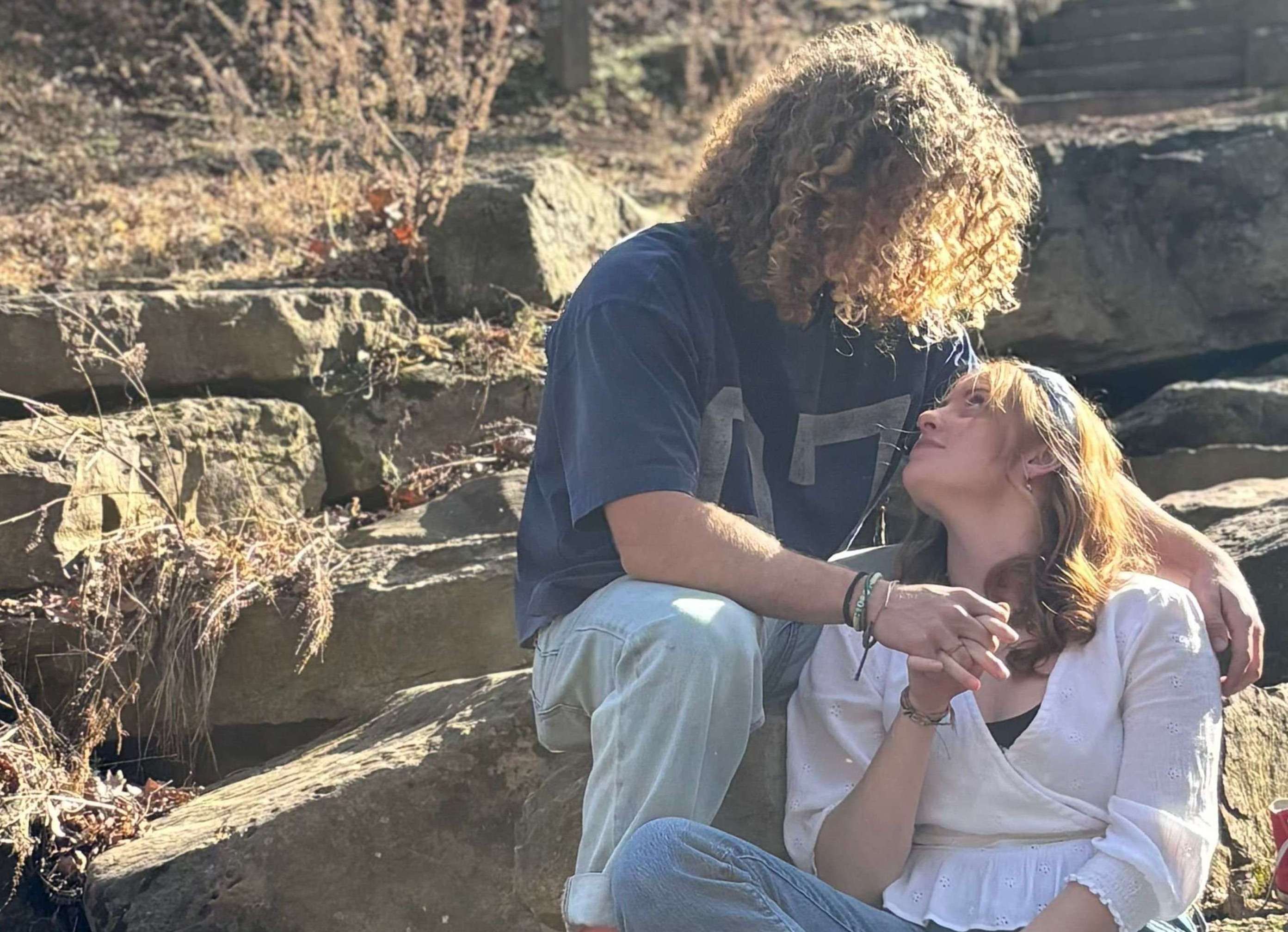 a man and a woman sitting on rocks in a wooded area