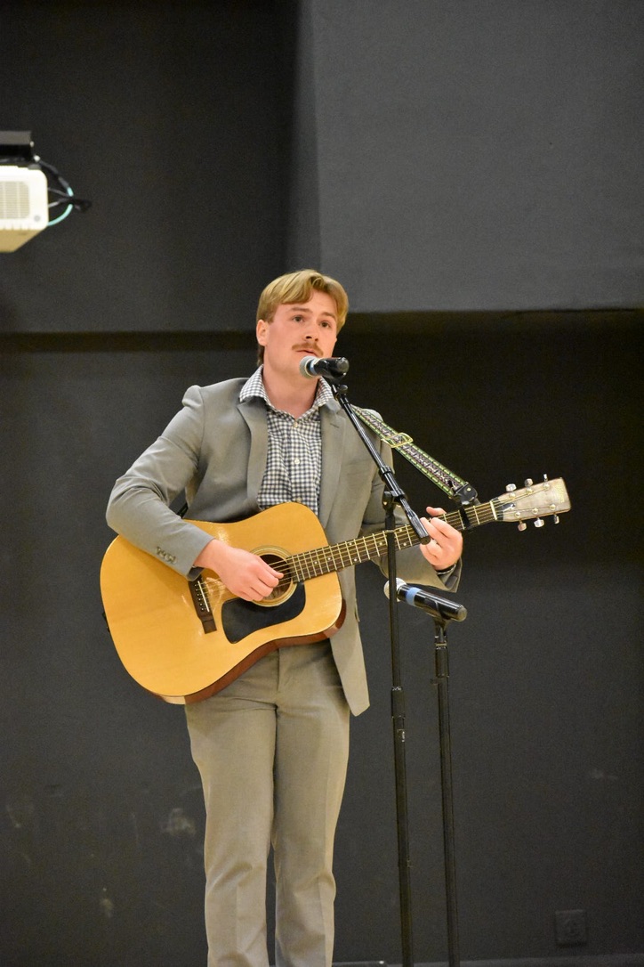 a man singing into a microphone with an acoustic guitar