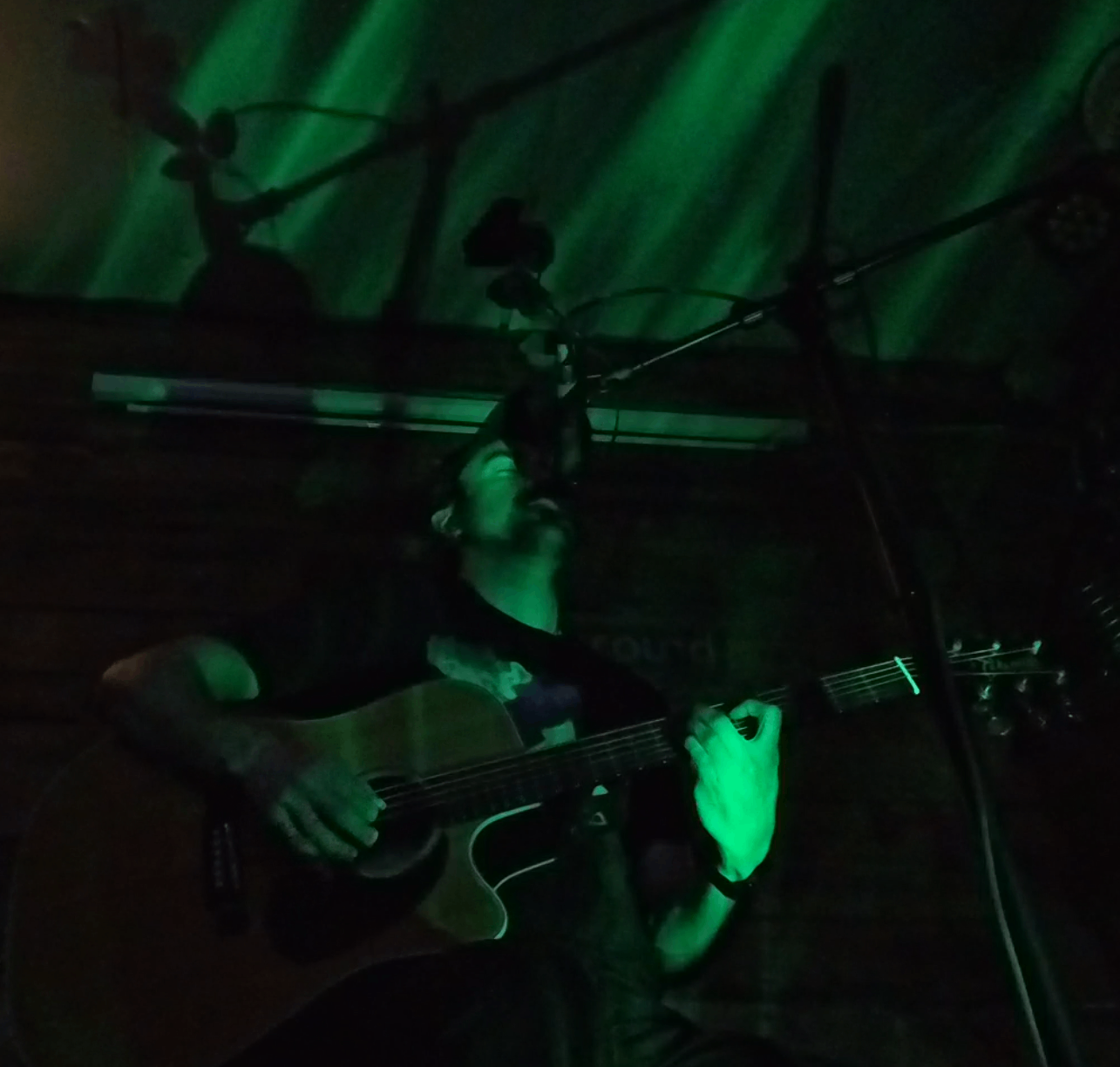 a man playing an acoustic guitar in front of a green light