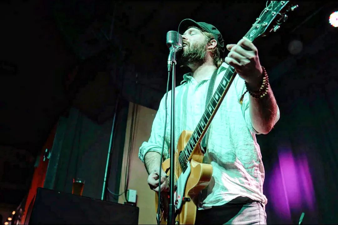 a man with a beard playing a guitar in front of a microphone