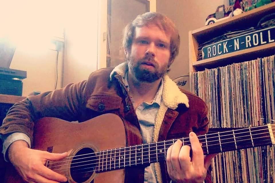 a man playing an acoustic guitar in front of records