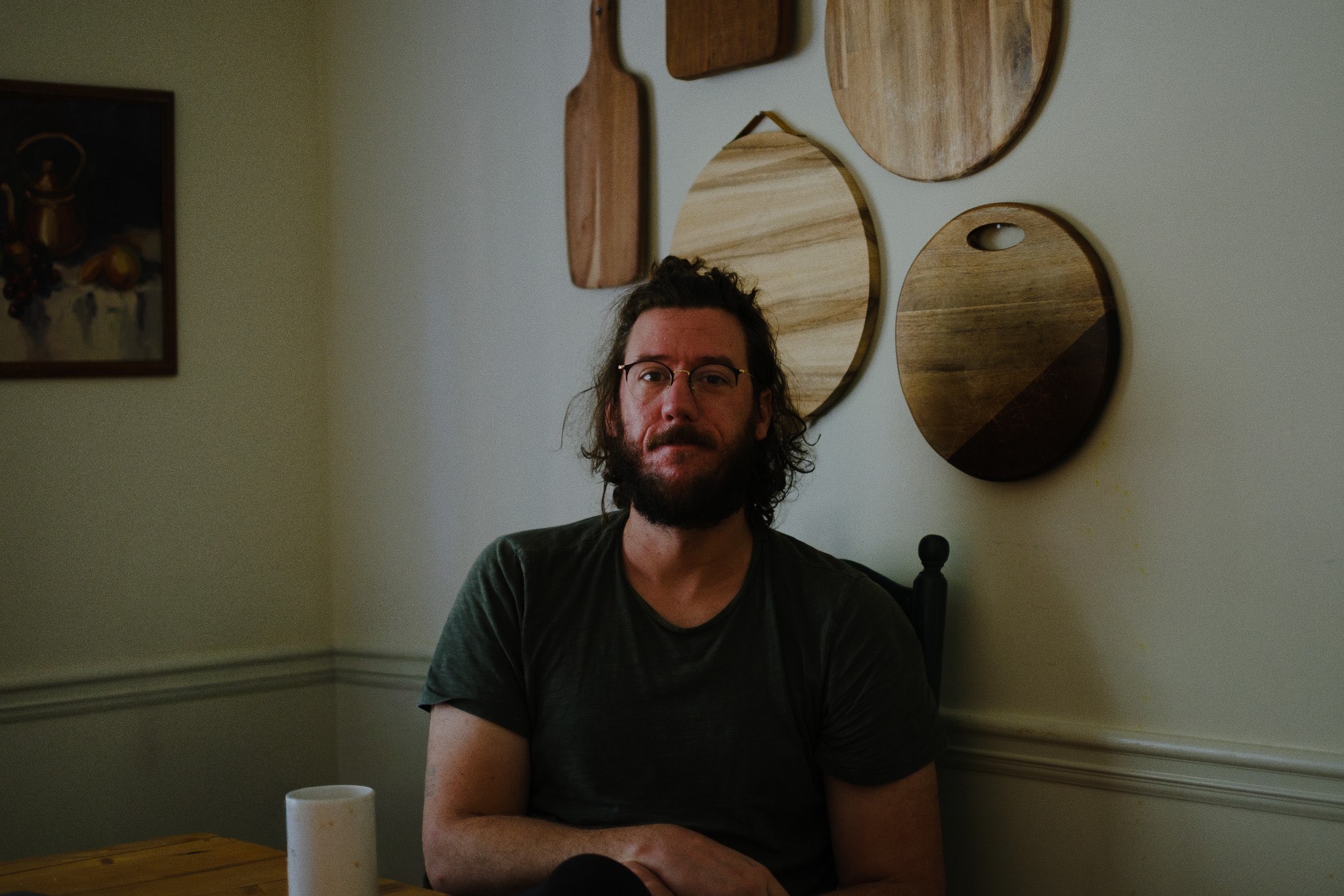 a man sitting at a table with several wooden cutting boards on the wall