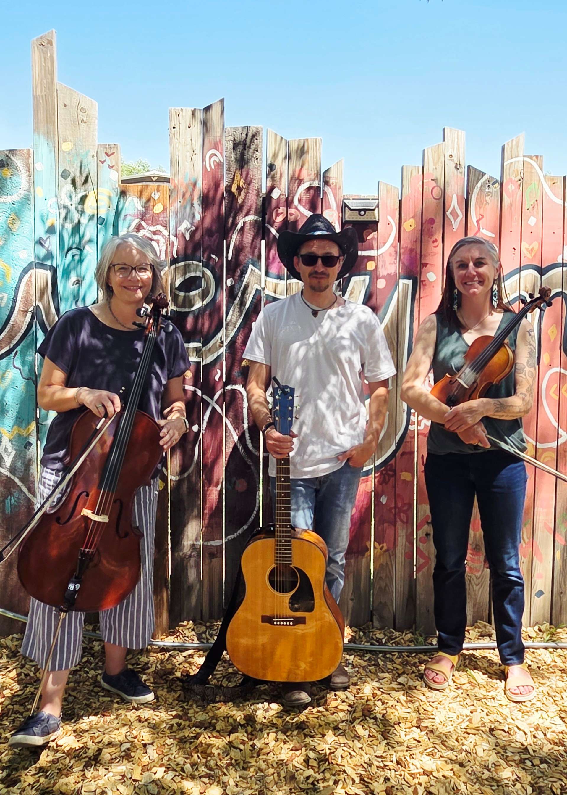 three people standing in front of a fence with guitars