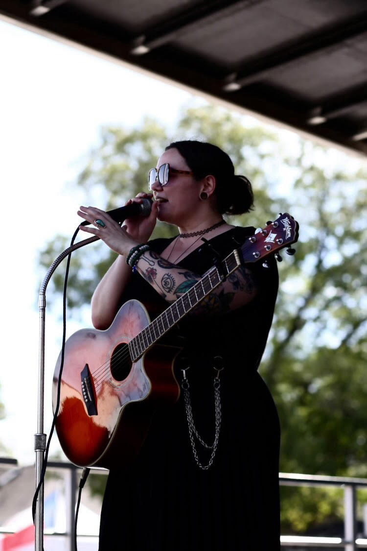 a woman singing into a microphone while holding an acoustic guitar