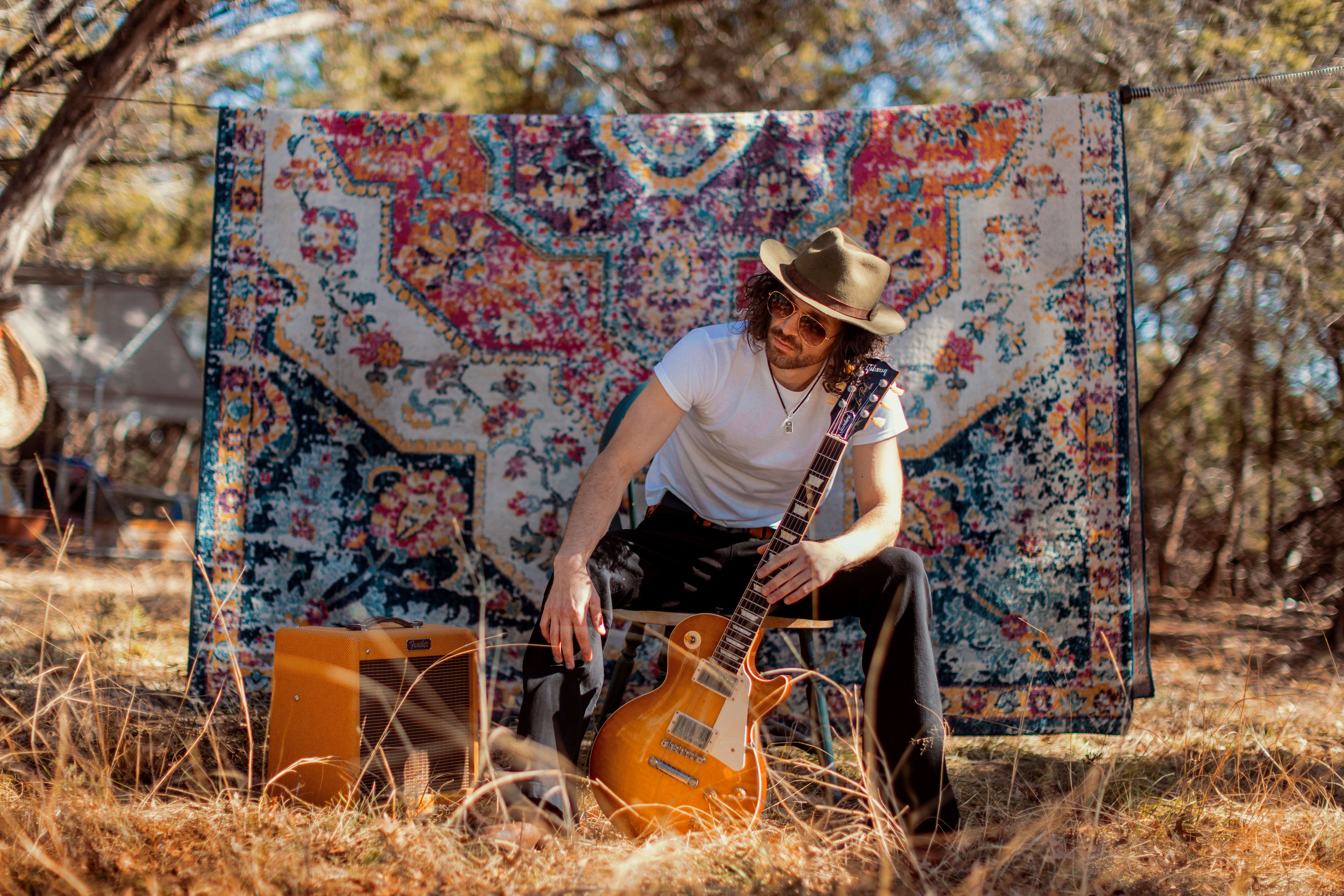 a man with a guitar sitting on a blanket in a field