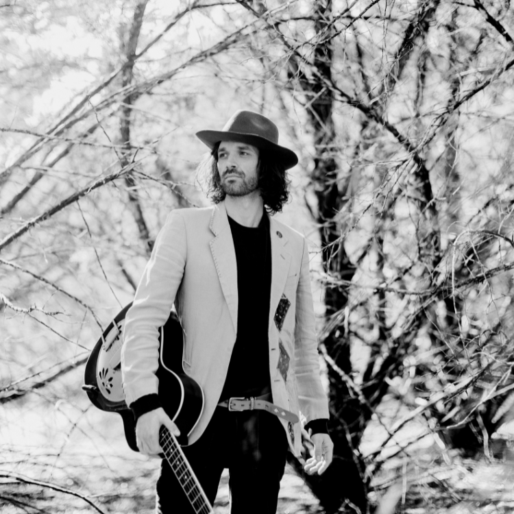 a man holding a guitar in the woods